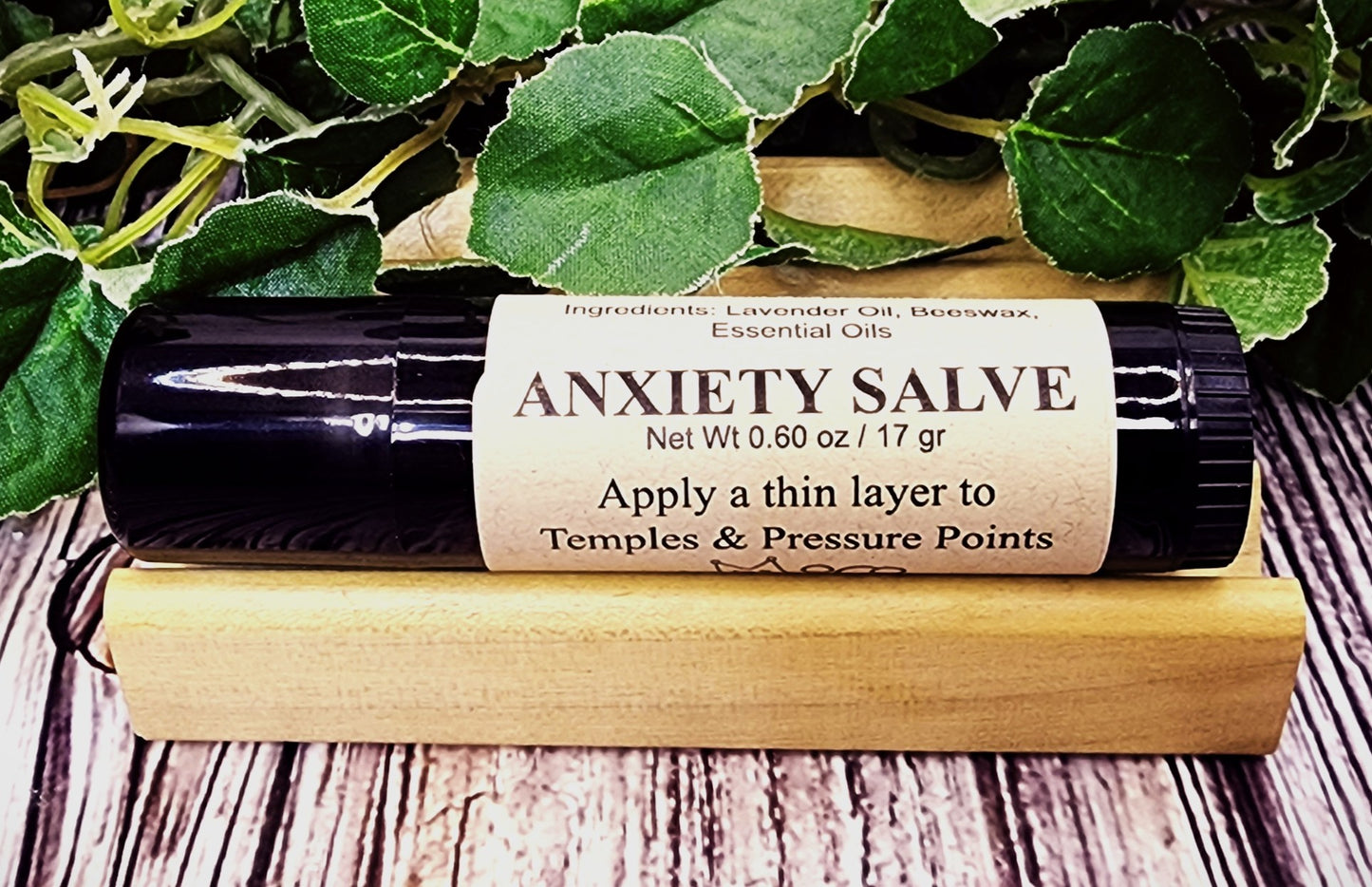 Anxiety salve roll-on with label and wooden applicator on a wooden surface with green leaves.
