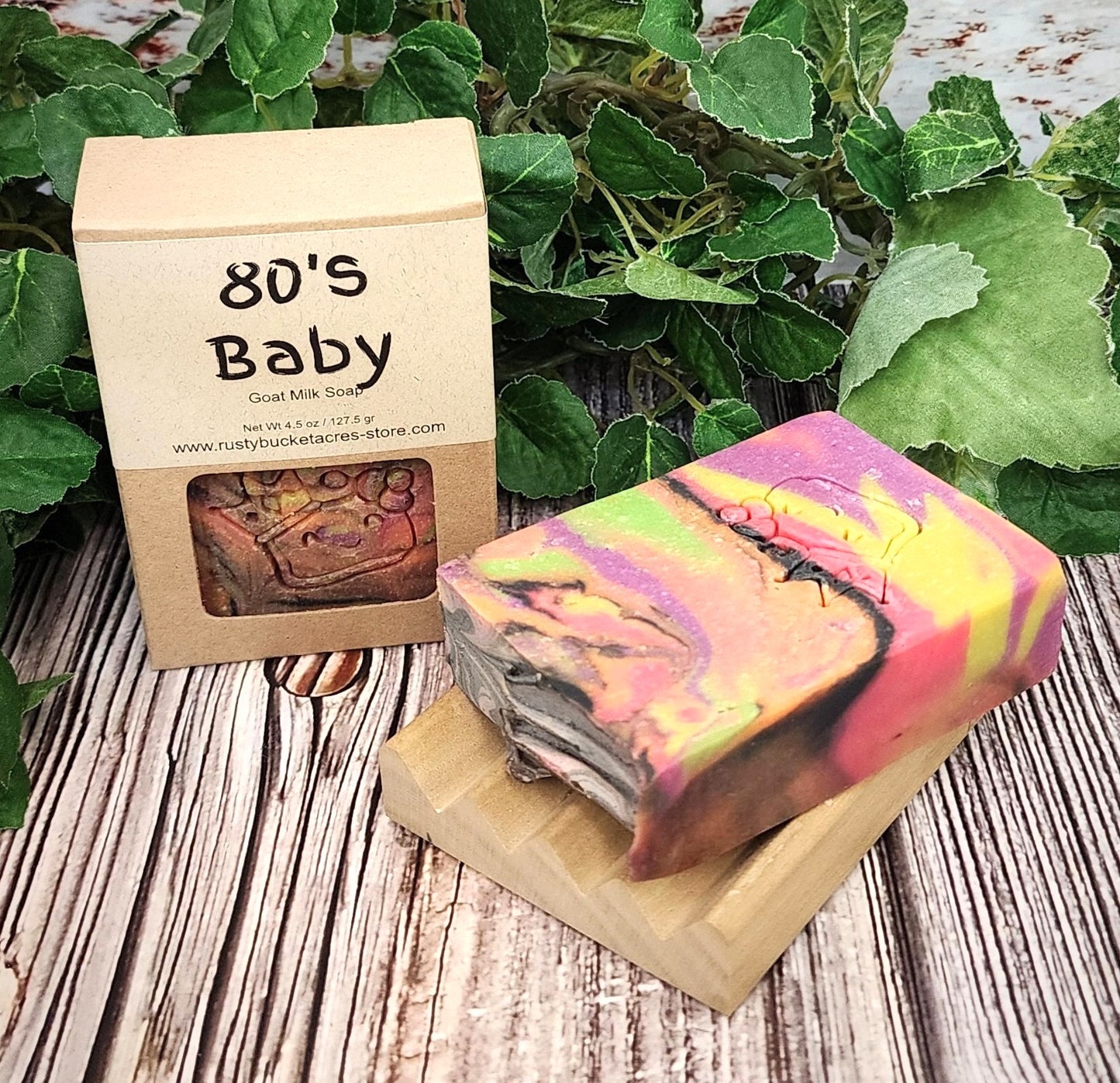 Colorful soap bar with '80's Baby' packaging on a wooden surface with green leaves in the background