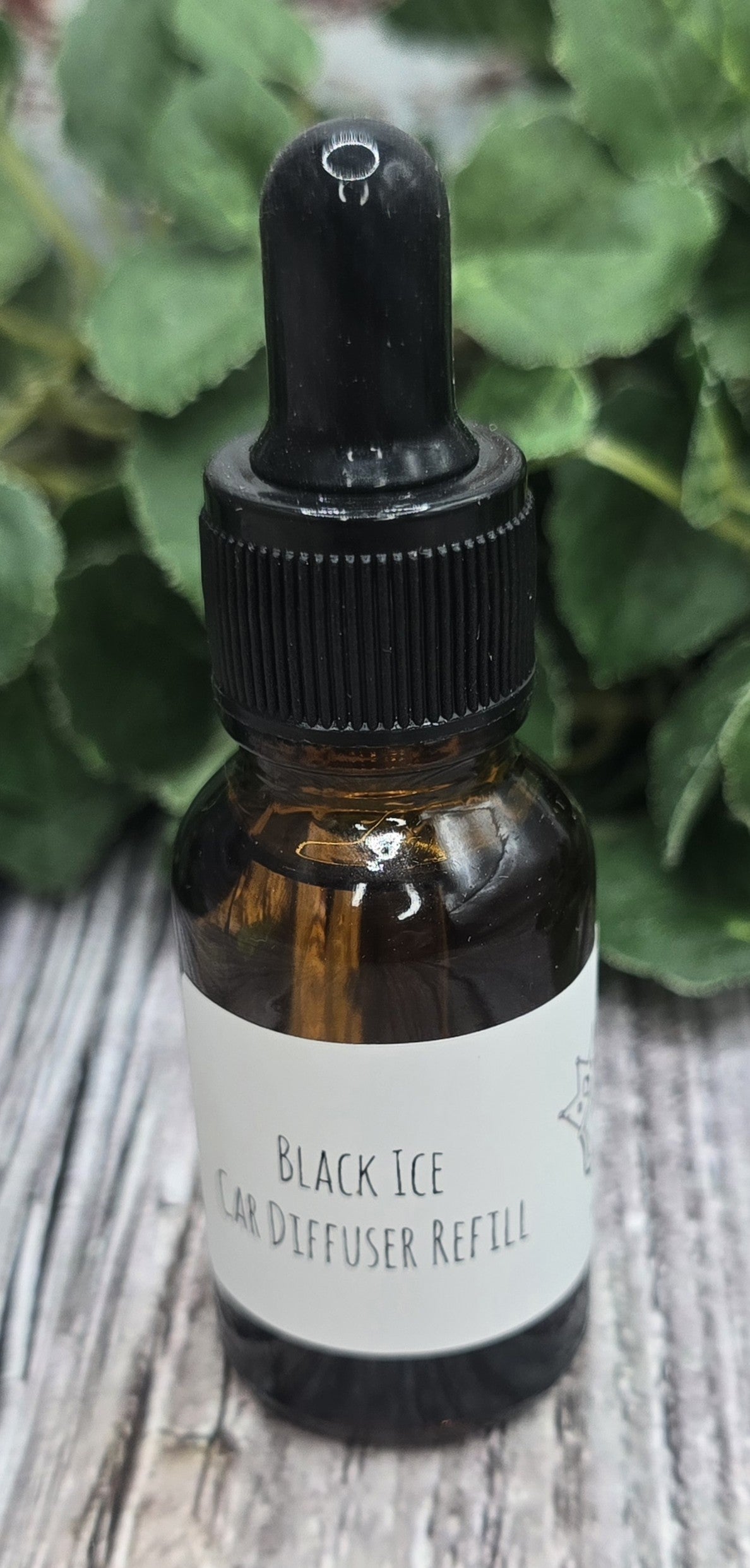 Bottle of Black Ice car diffuser refill with a dropper on a wooden surface with greenery in the background.