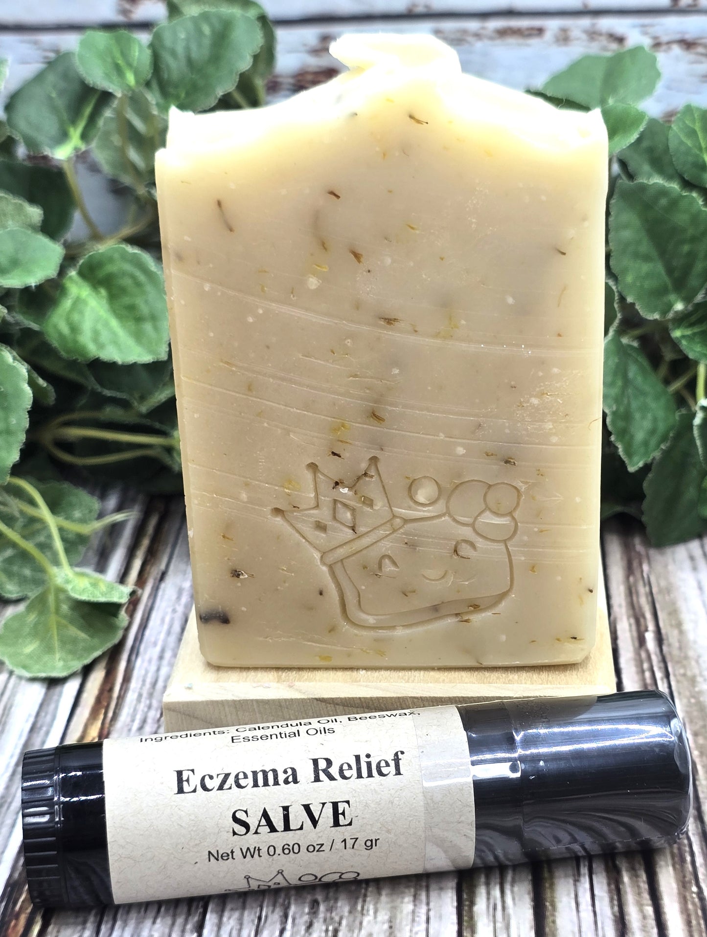Bar of soap with a small tube of eczema relief salve on a wooden surface with green leaves in the background.