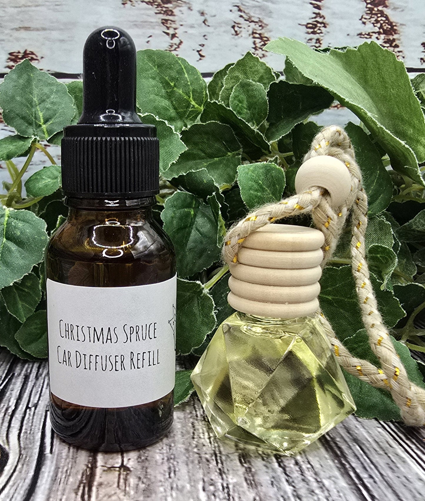 Two bottles of 'Christmas Spruce' car diffuser refills on a wooden surface with green leaves in the background.