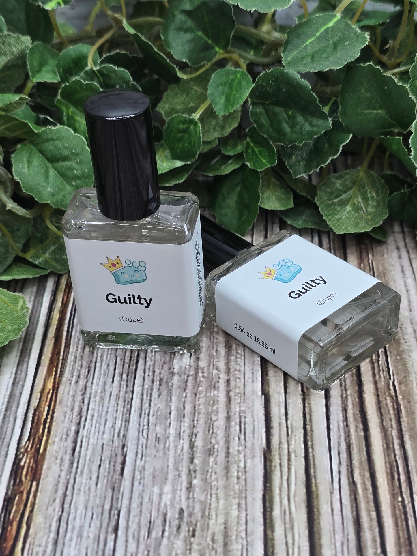 Two small bottles labeled 'Guilty' on a wooden surface with green leaves.