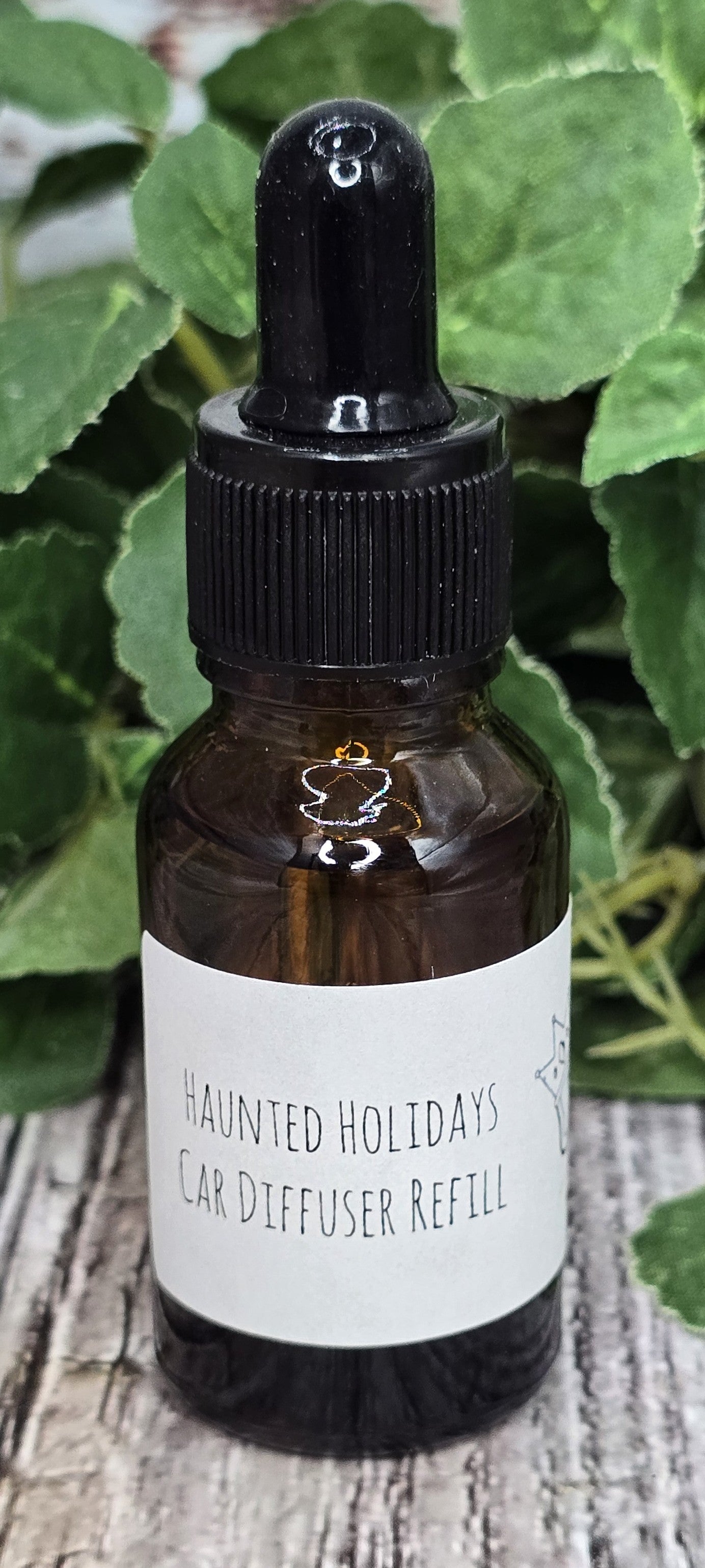 Bottle of 'Haunted Holidays' ear diffuser refill with a dropper on a wooden surface with green leaves in the background.