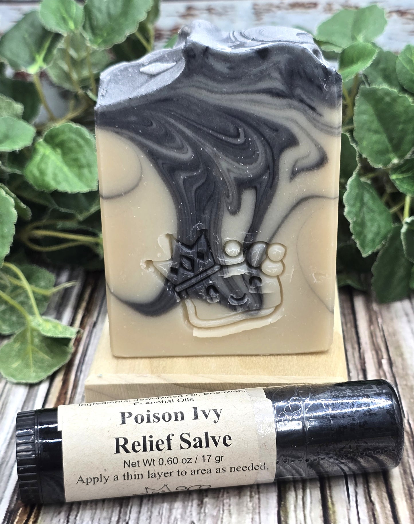 Bar of soap with black and white swirls and a bottle of Poison Ivy Relief Salve on a wooden surface with green leaves.