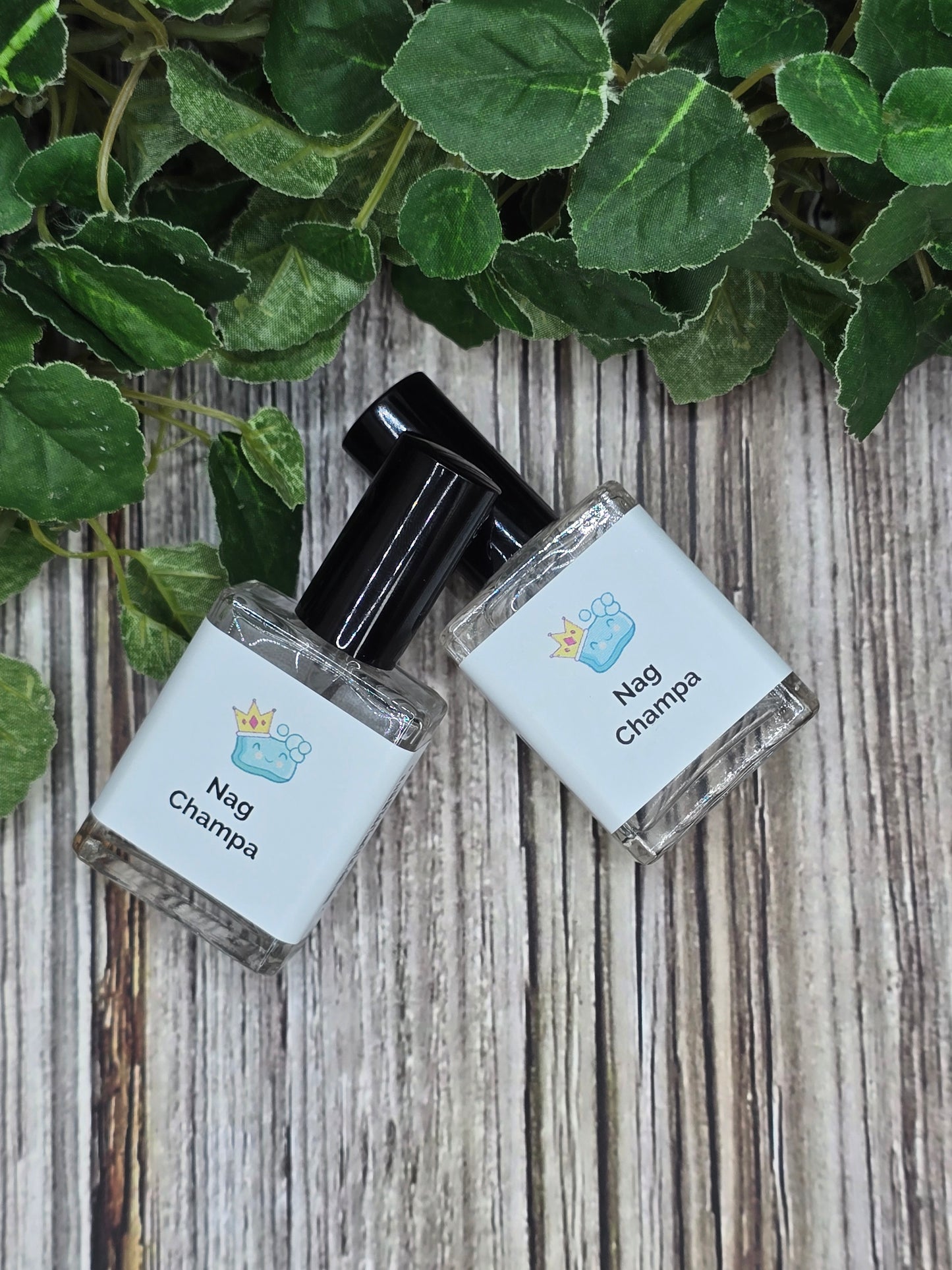 Two small bottles of Nag Champa perfume on a wooden surface with green leaves.