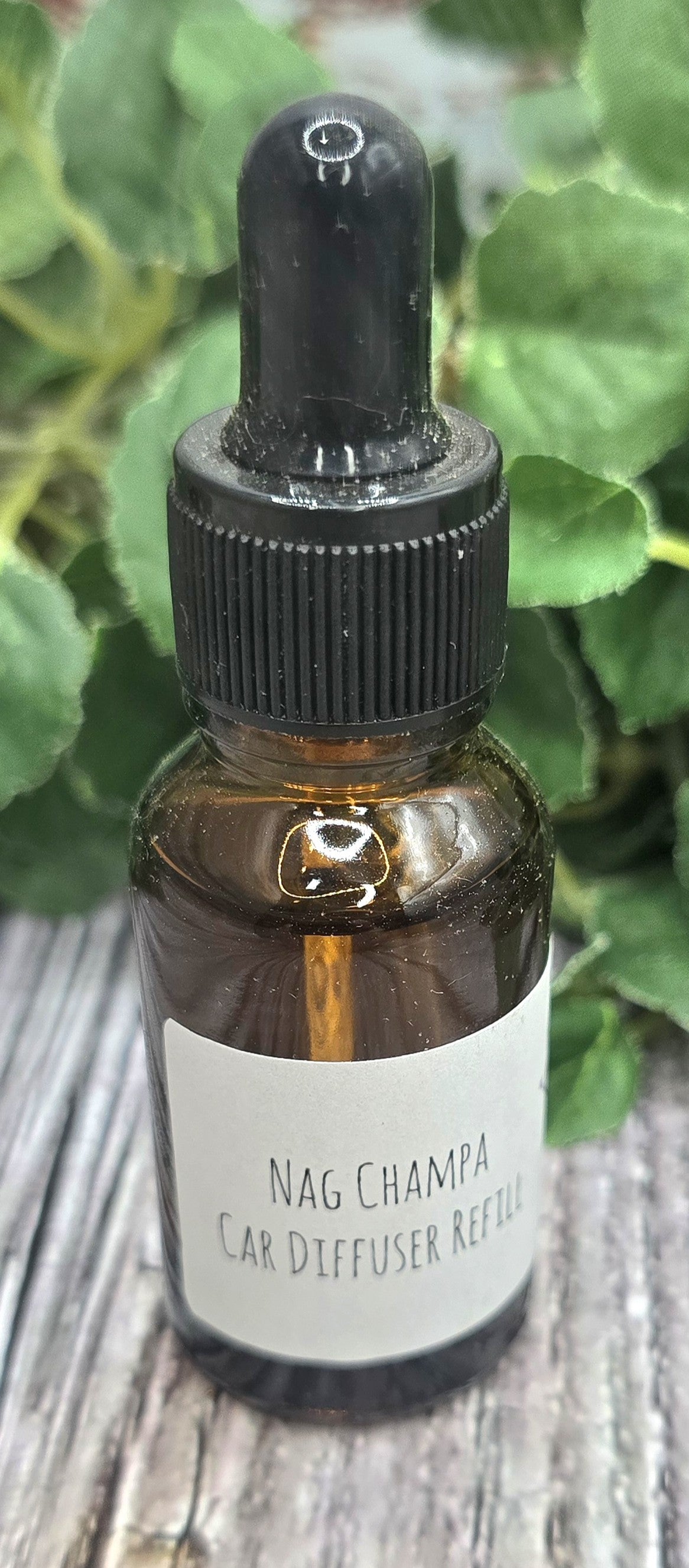 Bottle of Nag Champa essential oil with a dropper on a wooden surface with green leaves in the background