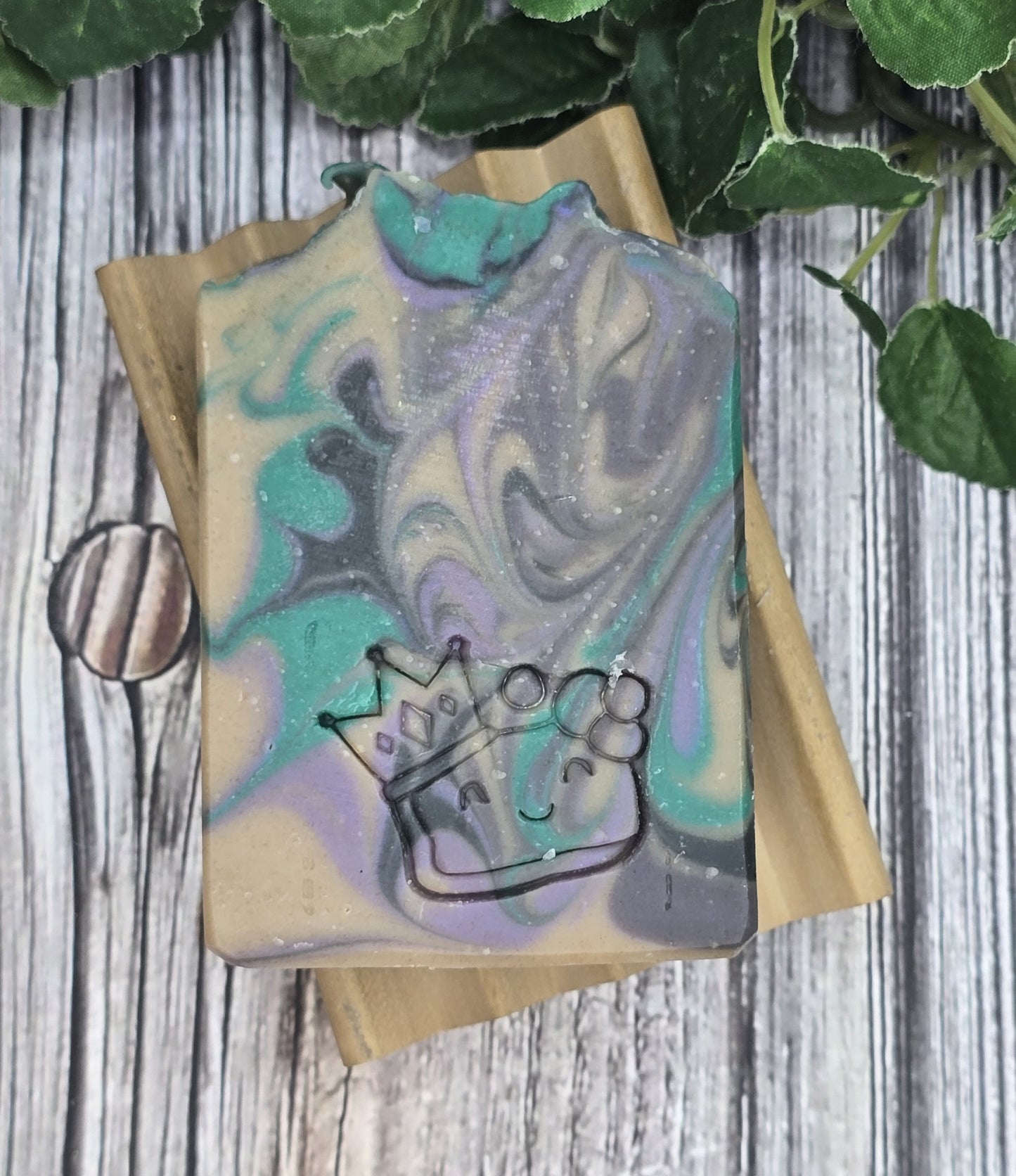 Marbled soap bar with a crown design on a wooden block, surrounded by green leaves.