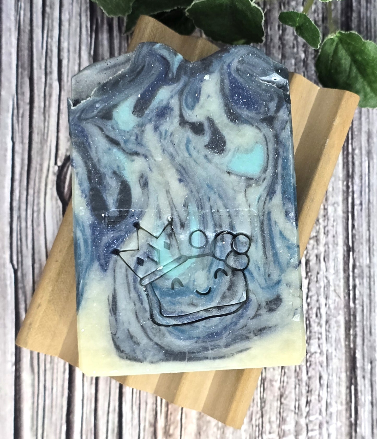 Marbled blue and gray soap bar with a smiley face and crown on a wooden block.