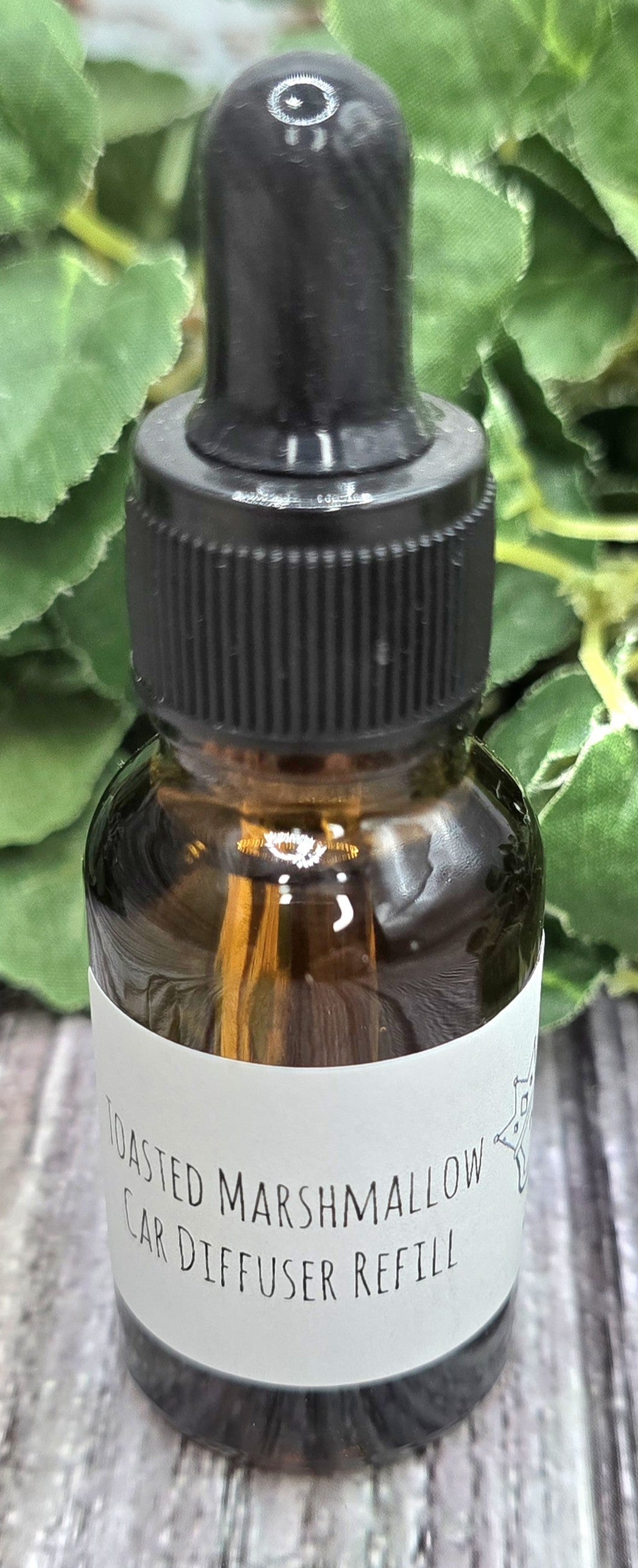 Brown glass bottle with dropper labeled 'Toasted Marshmallow' on a wooden surface with green leaves in the background