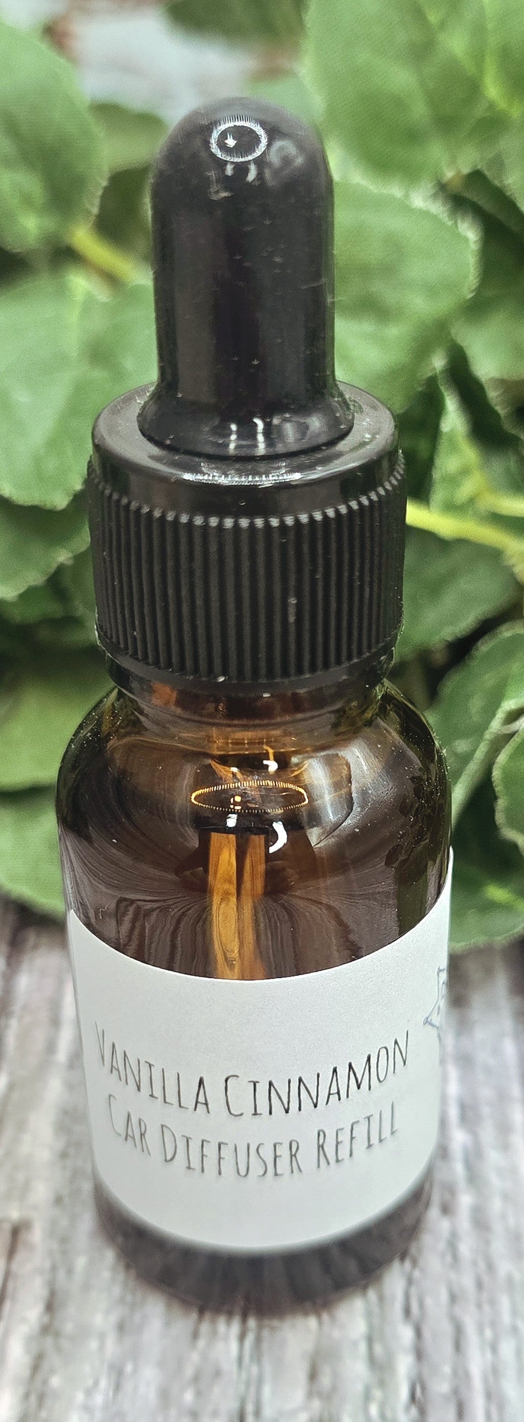 Vanilla Cinnamon diffuser refill bottle with dropper on a wooden surface with green leaves in the background