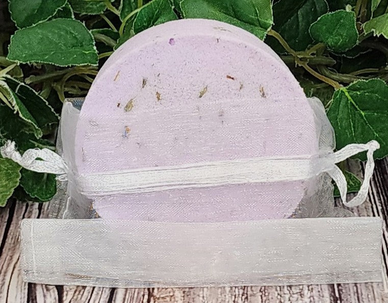 Purple bath bomb in a clear plastic bag with green leaves in the background
