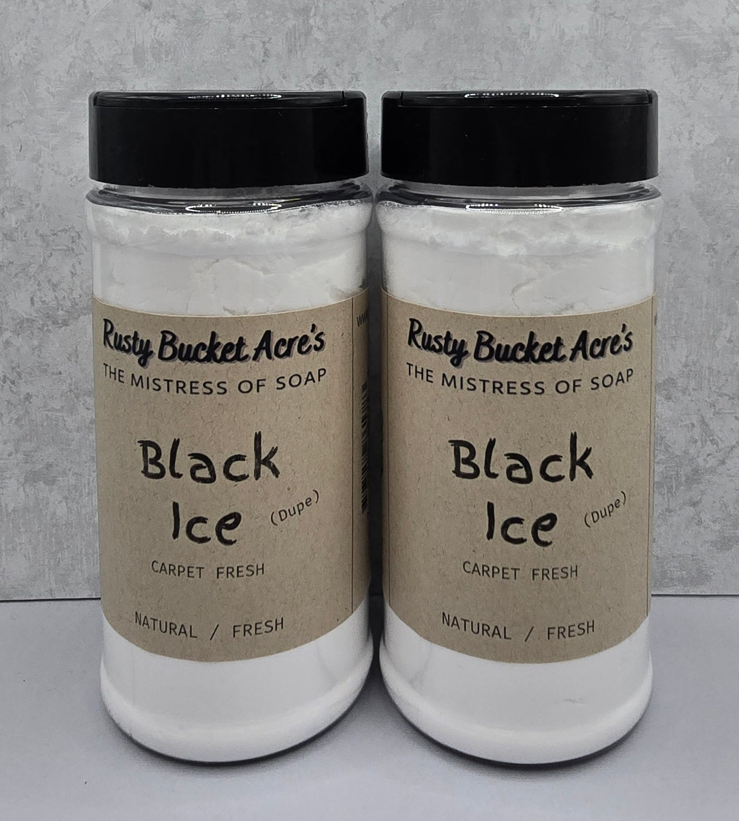 Two clear plastic jars of Rusty Bucket Acre's Black Ice Carpet Fresh soap, filled with white soap and topped with black lids, set against a textured gray background.