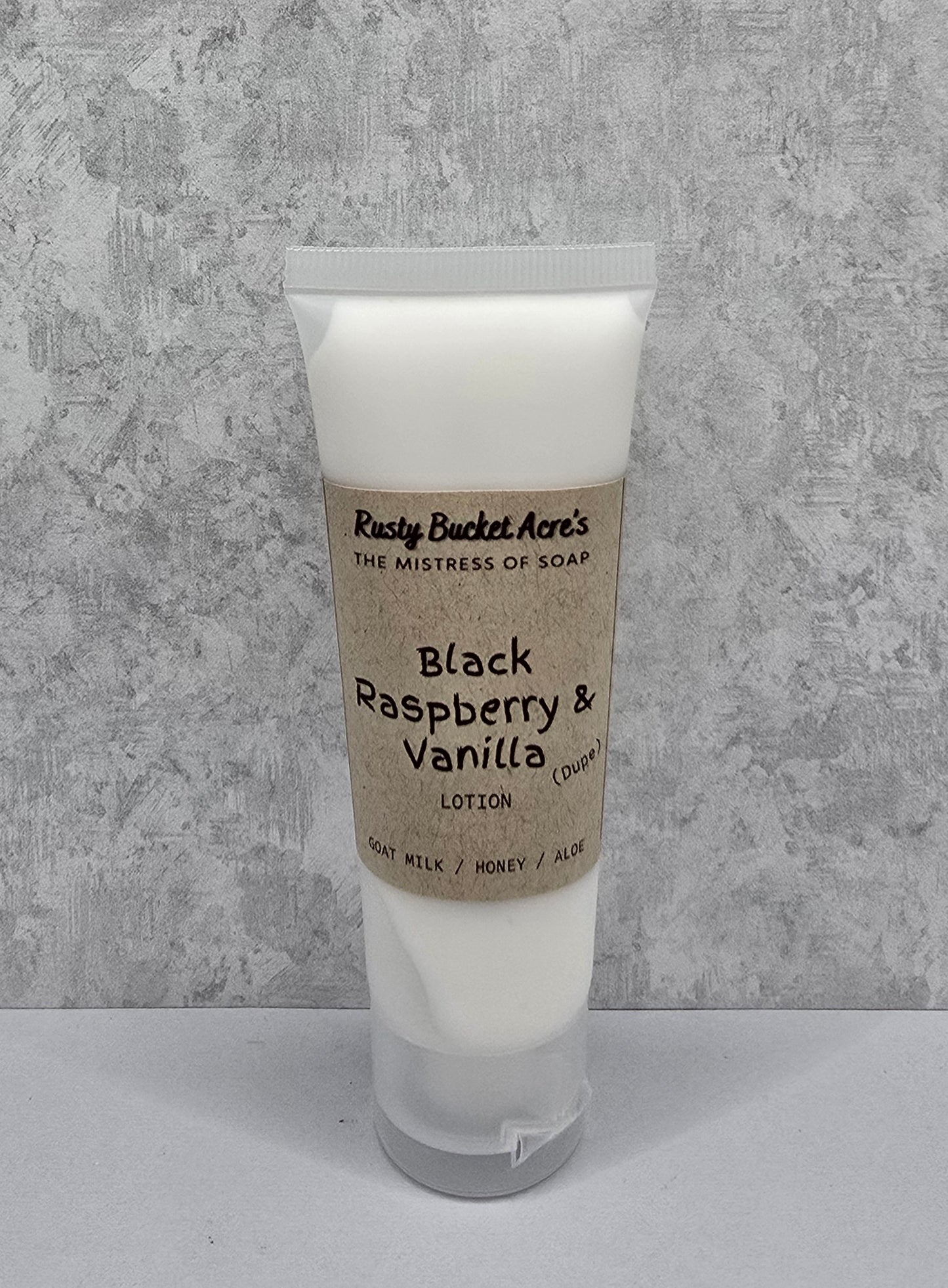 Tube of Black Raspberry & Vanilla Dupe lotion with a kraft paper label on a gray background
