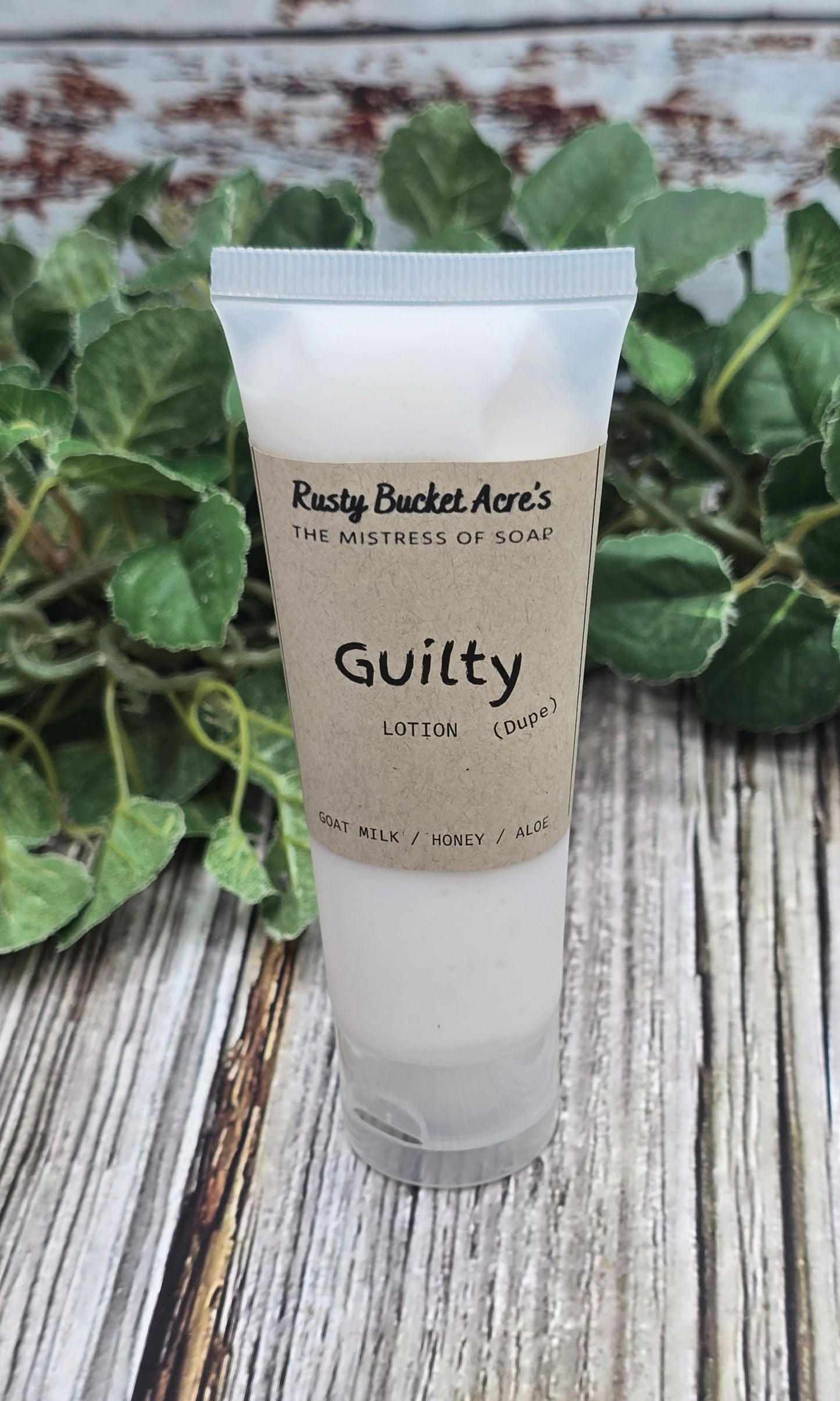Tube of 'Guilty' lotion from Rusty Bucket Acres on a wooden surface with greenery.