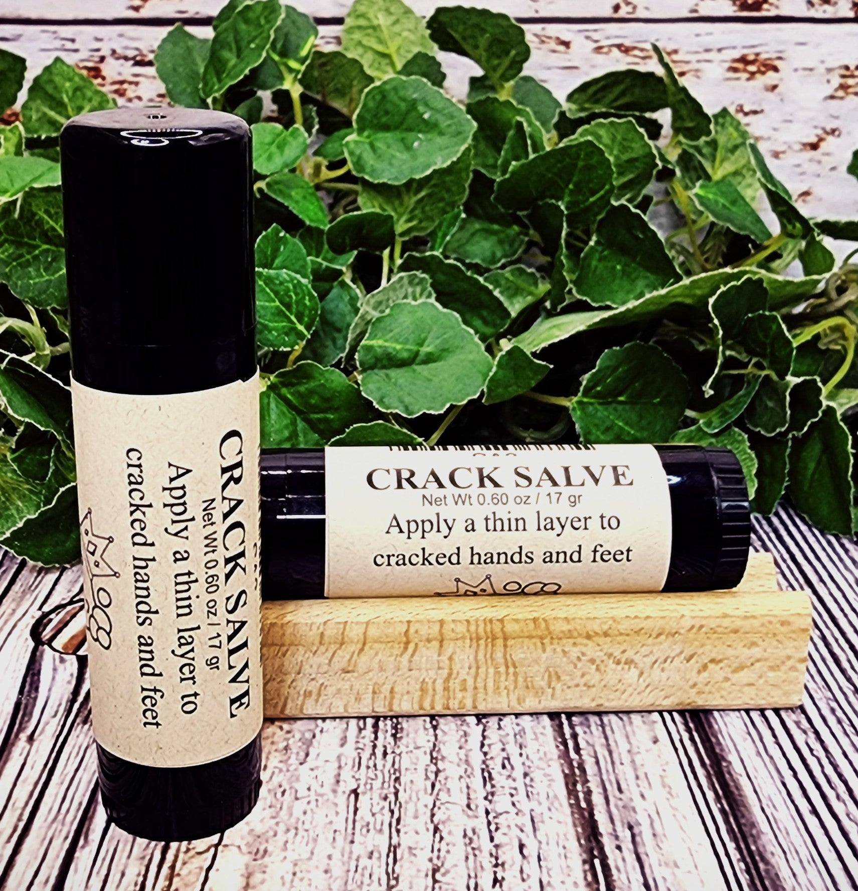 Two bottles of Crack Salve on a wooden surface with green leaves in the background