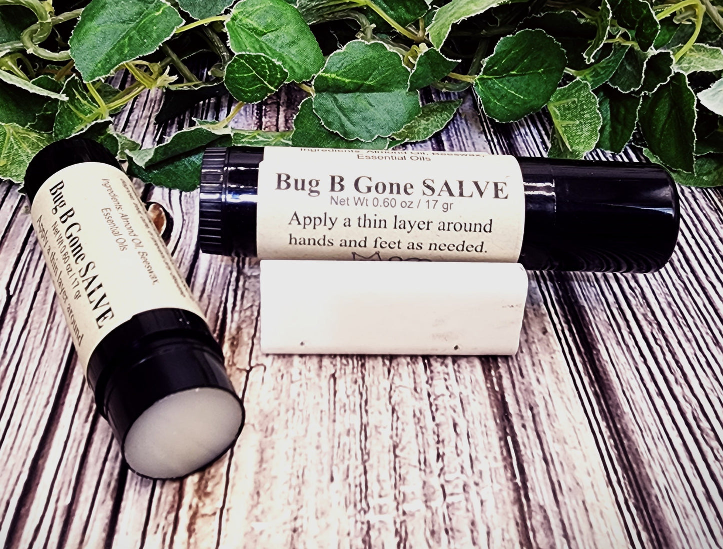 Bug B Gone Salve with packaging on a wooden surface with green leaves in the background