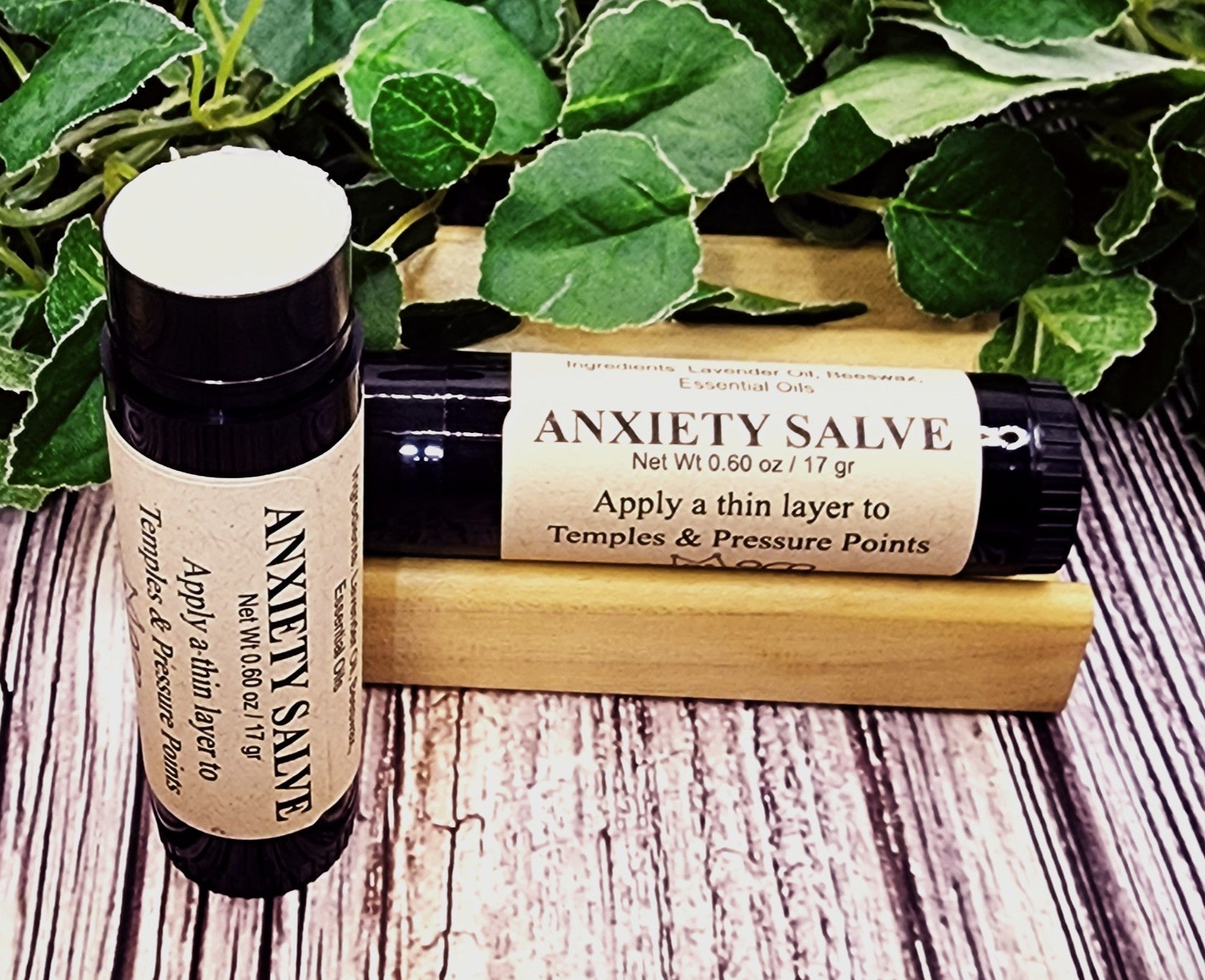 Two bottles of Anxiety Salve on a wooden surface with green leaves in the background