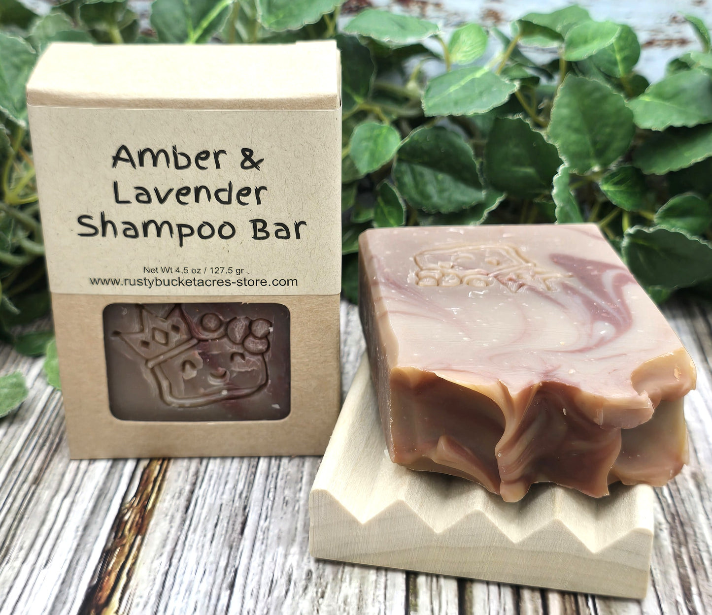 Amber & Lavender Shampoo Bar with packaging on a wooden surface with greenery in the background