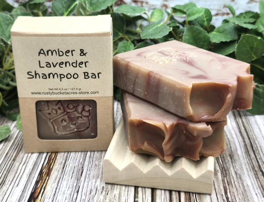 Amber & Lavender Shampoo Bar with packaging on a wooden surface with greenery in the background