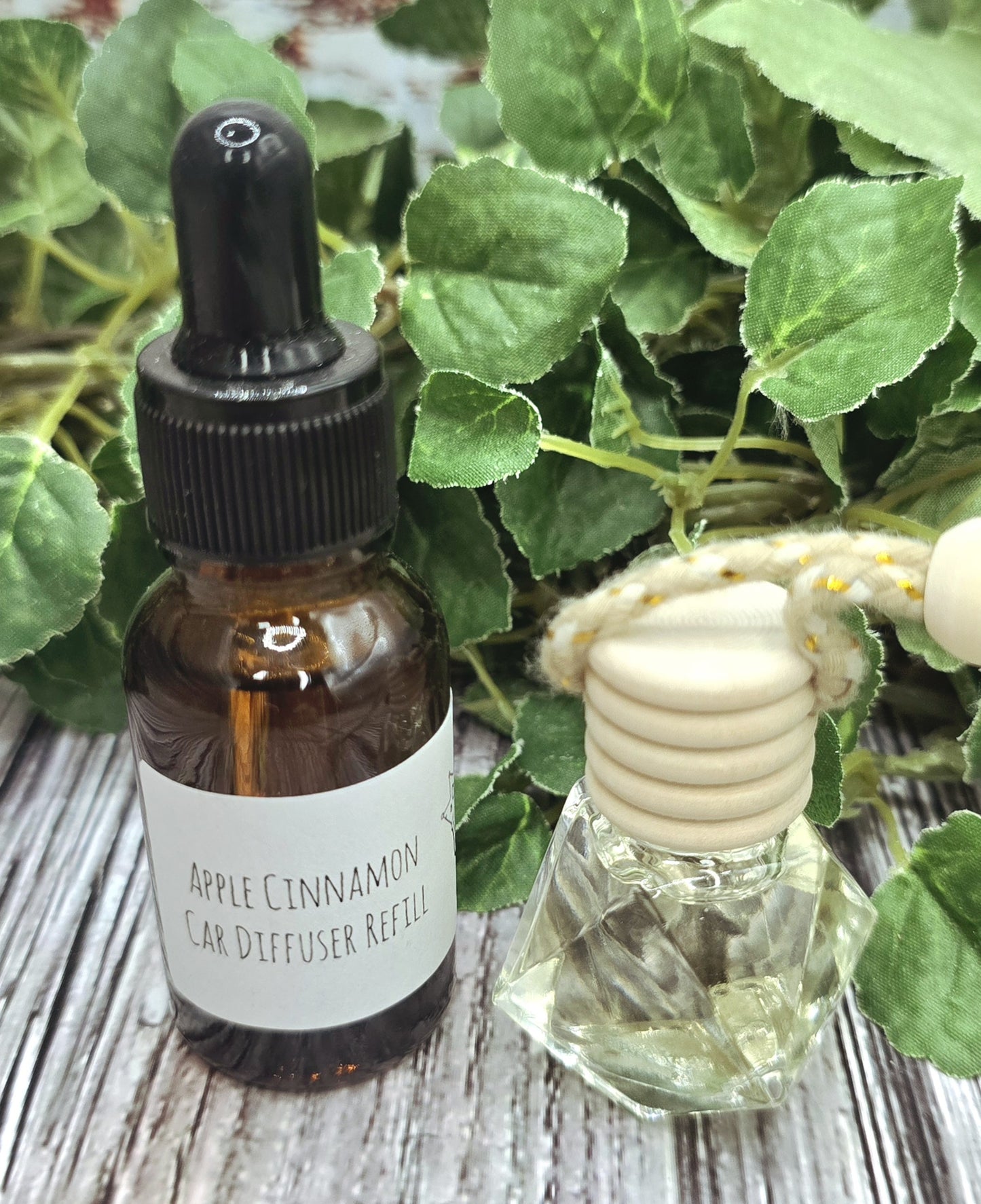 Bottle of Apple Cinnamon Car Diffuser Refill with a clear diffuser on a wooden surface with green leaves.