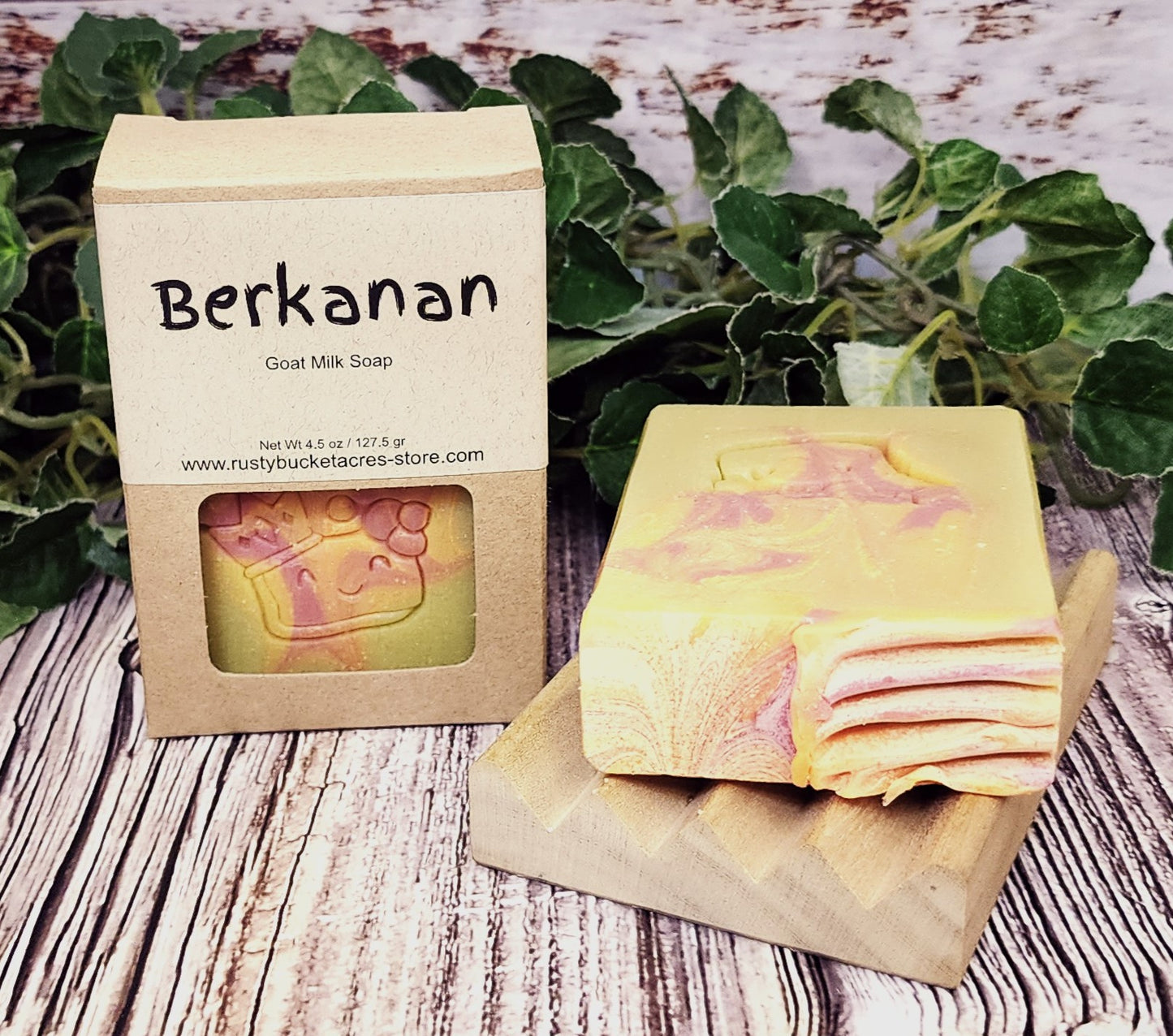 Goat milk soap with packaging labeled 'Berkanan' on a wooden surface with greenery in the background.