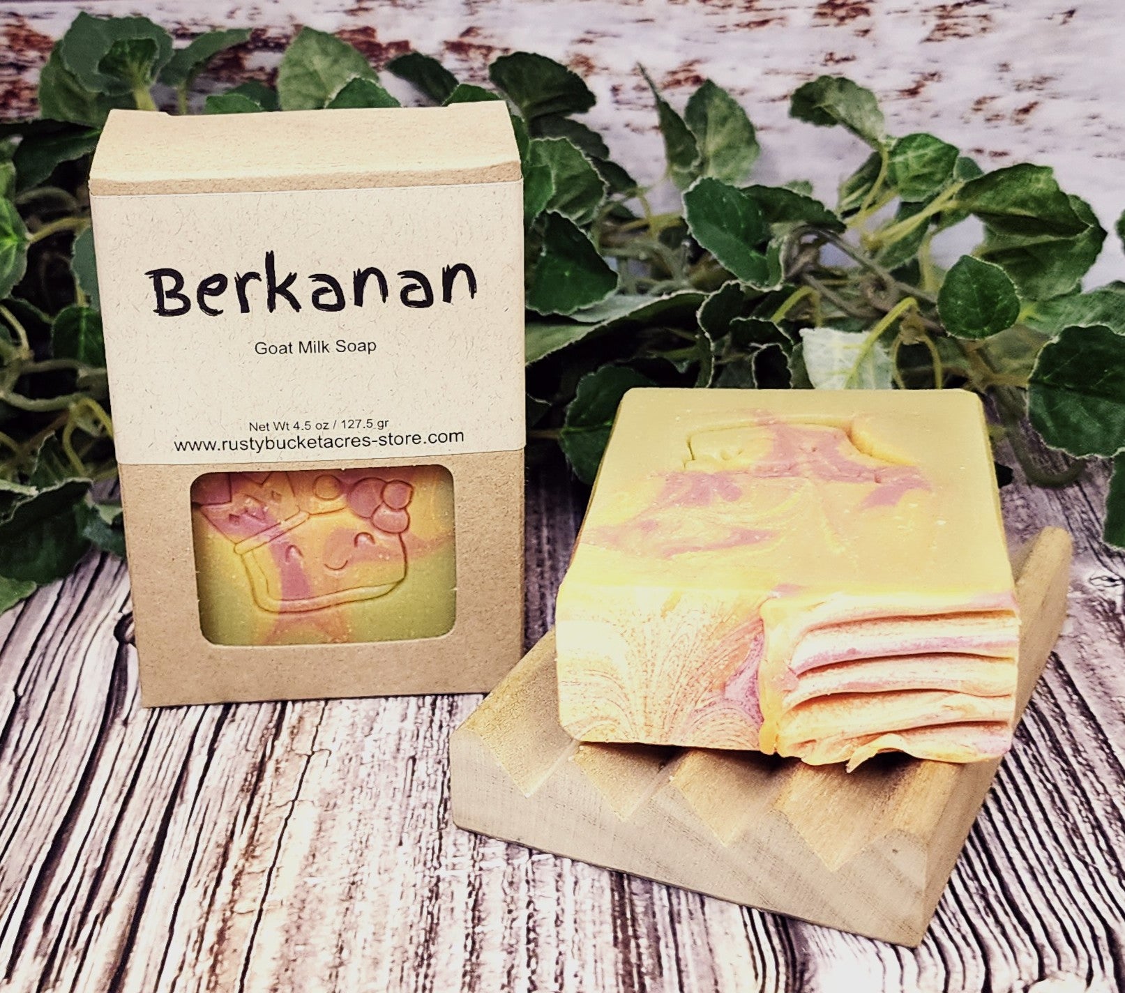 Goat milk soap with packaging labeled 'Berkanan' on a wooden surface with greenery in the background.