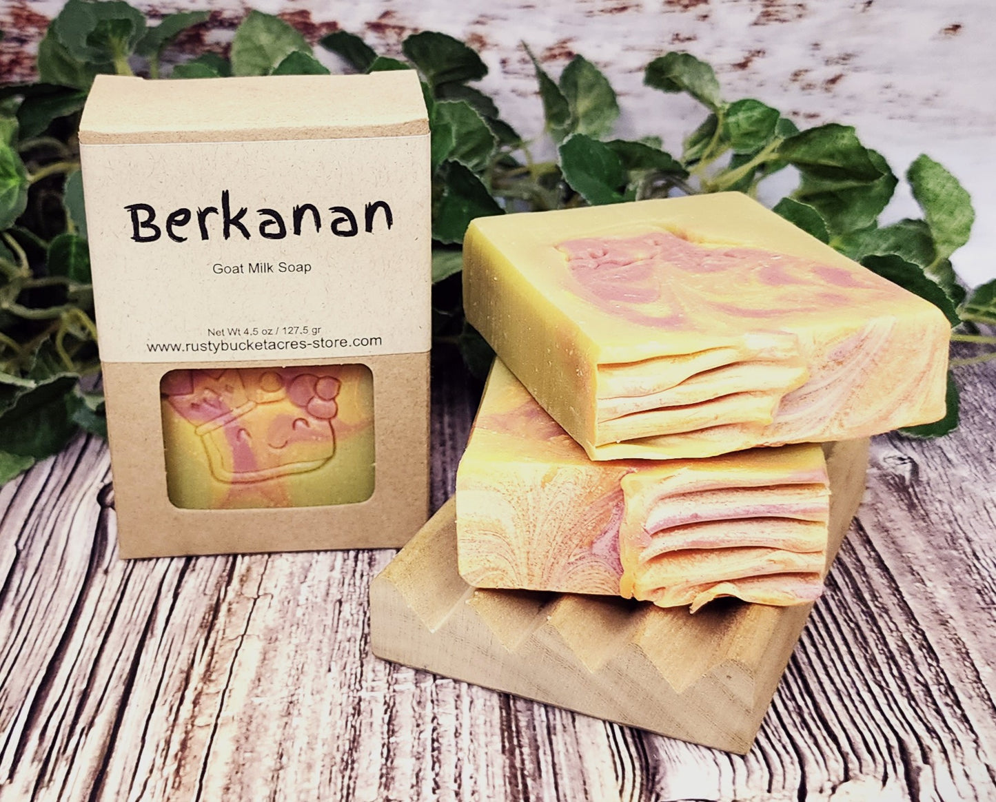 Two bars of soap with a 'Berkanan' packaging on a wooden surface with greenery in the background.