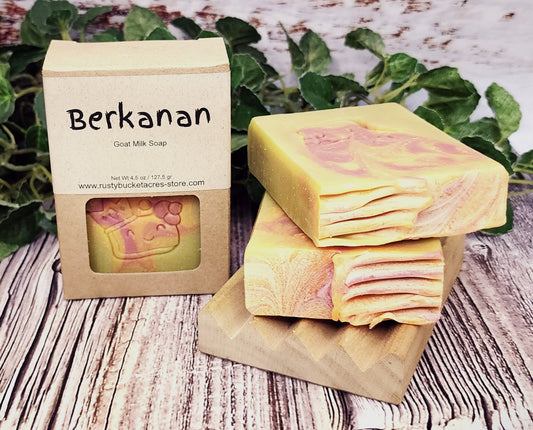 Two bars of soap with a 'Berkanan' packaging on a wooden surface with greenery in the background.