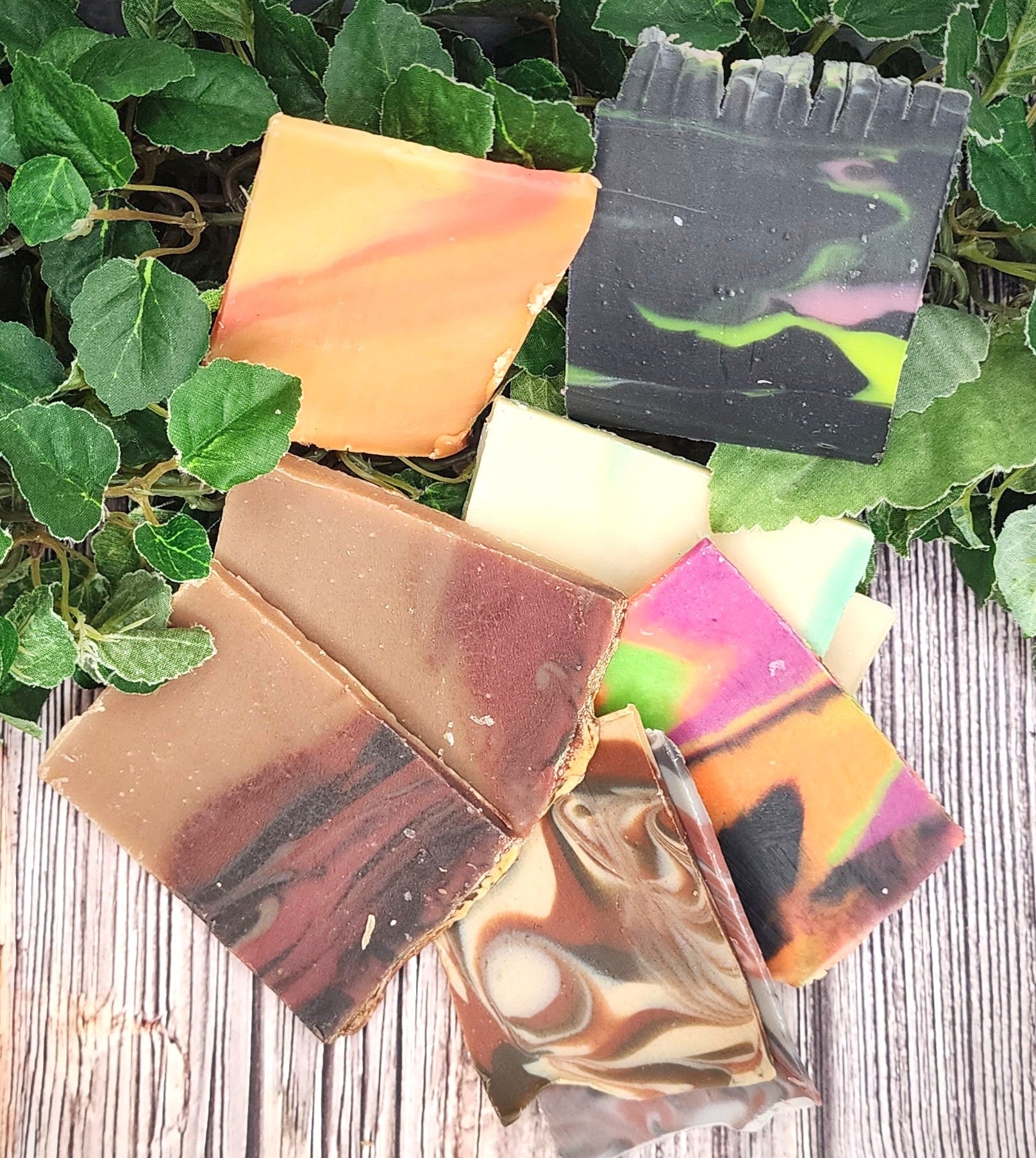 Colorful soap bars on a wooden surface with green leaves in the background