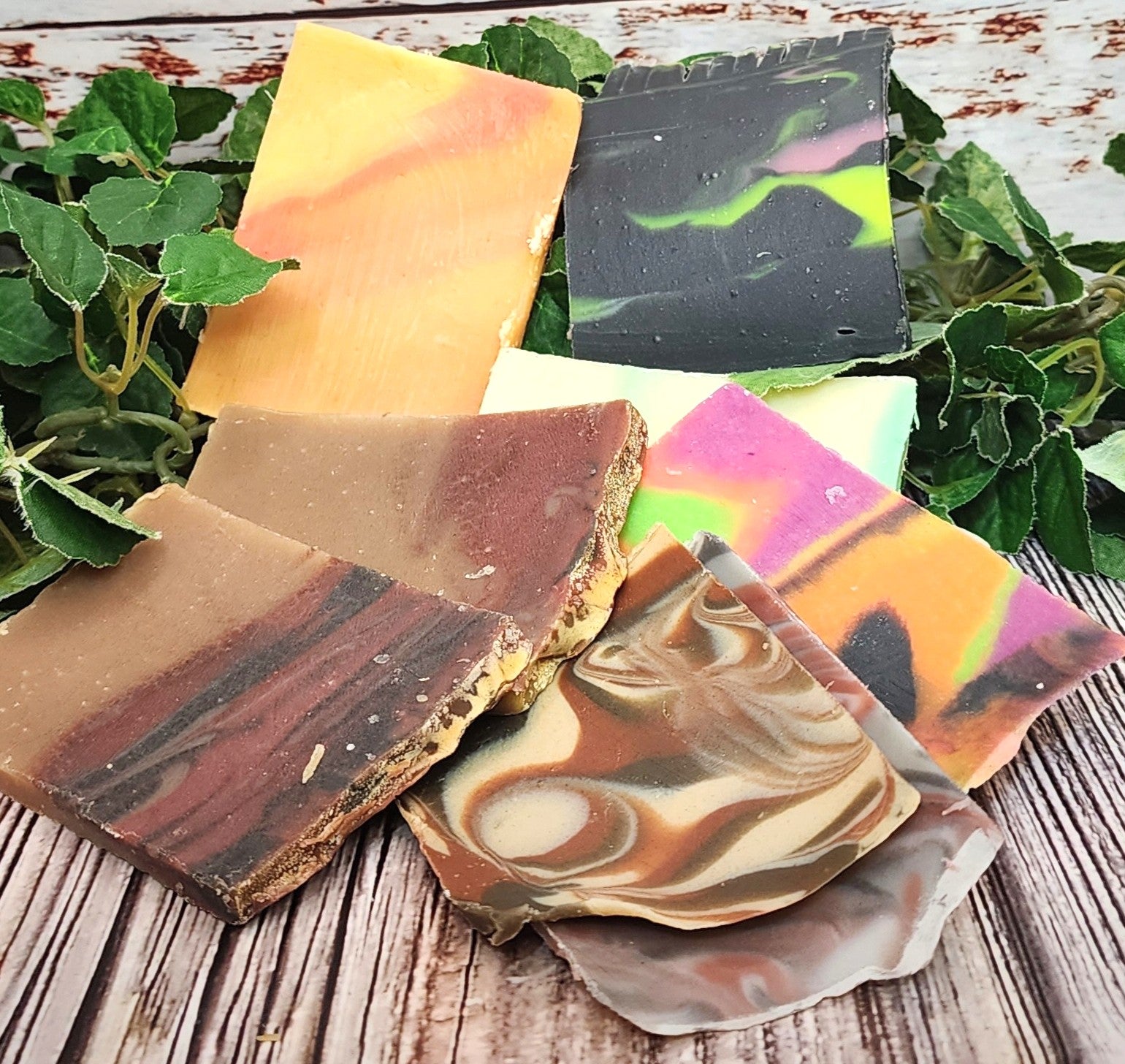Colorful soap bars with marbled patterns on a wooden surface with green leaves in the background