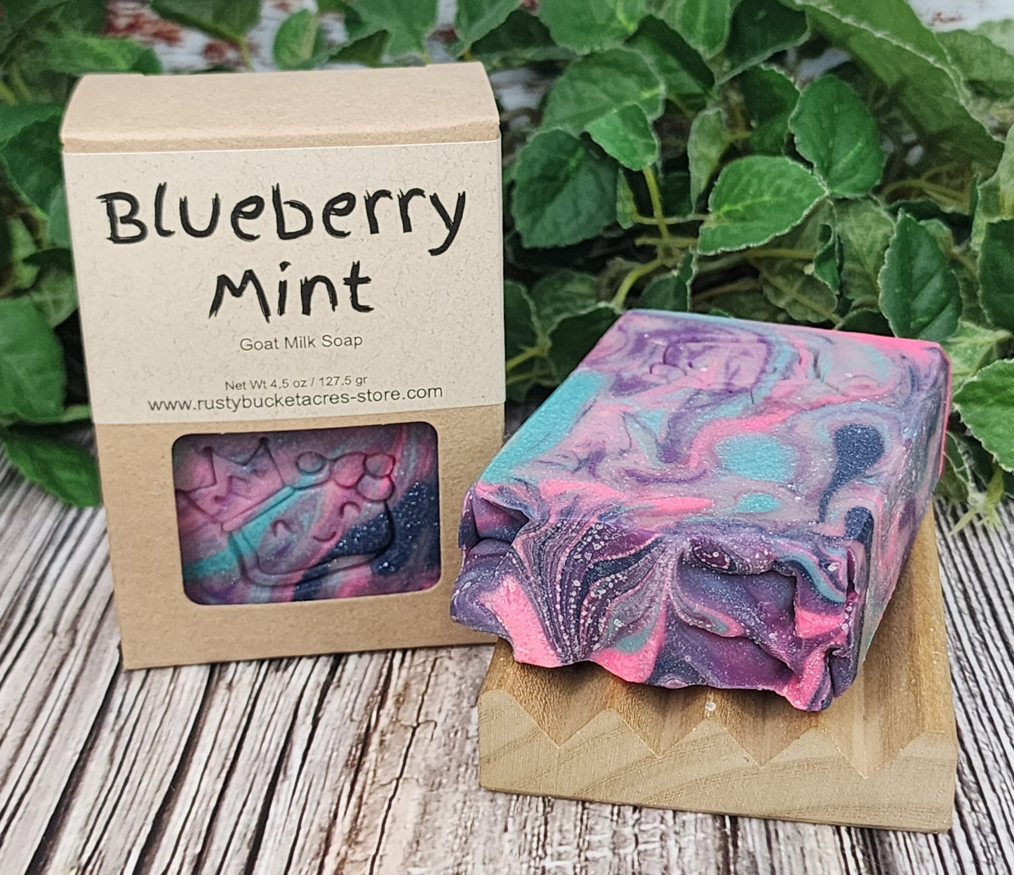 Blueberry Mint soap bar with packaging on a wooden surface with greenery in the background