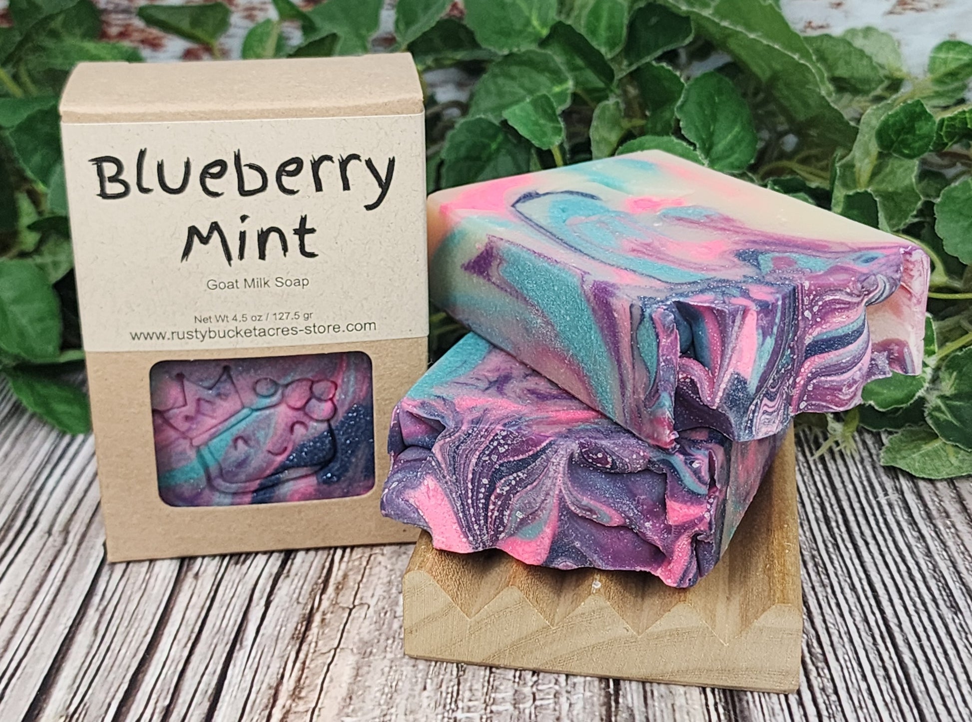 Marbled blueberry mint soap with a cardboard box on a wooden surface with greenery in the background