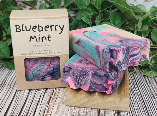 Marbled blueberry mint soap with a cardboard box on a wooden surface with greenery in the background