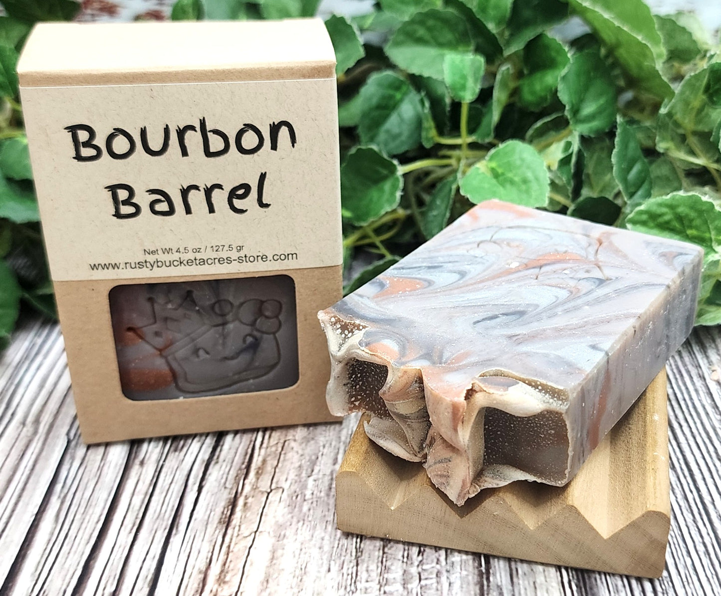 Bar of soap with a wooden box labeled 'Bourbon Barrel' on a wooden surface with greenery in the background.