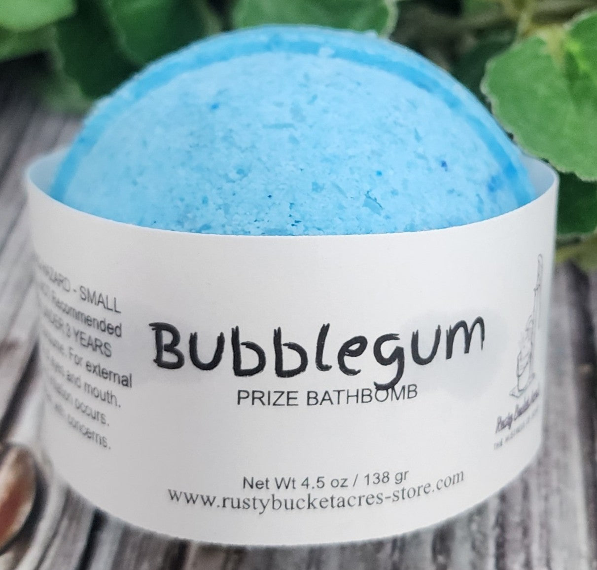 Blue bath bomb with a white label on a wooden surface with green leaves in the background