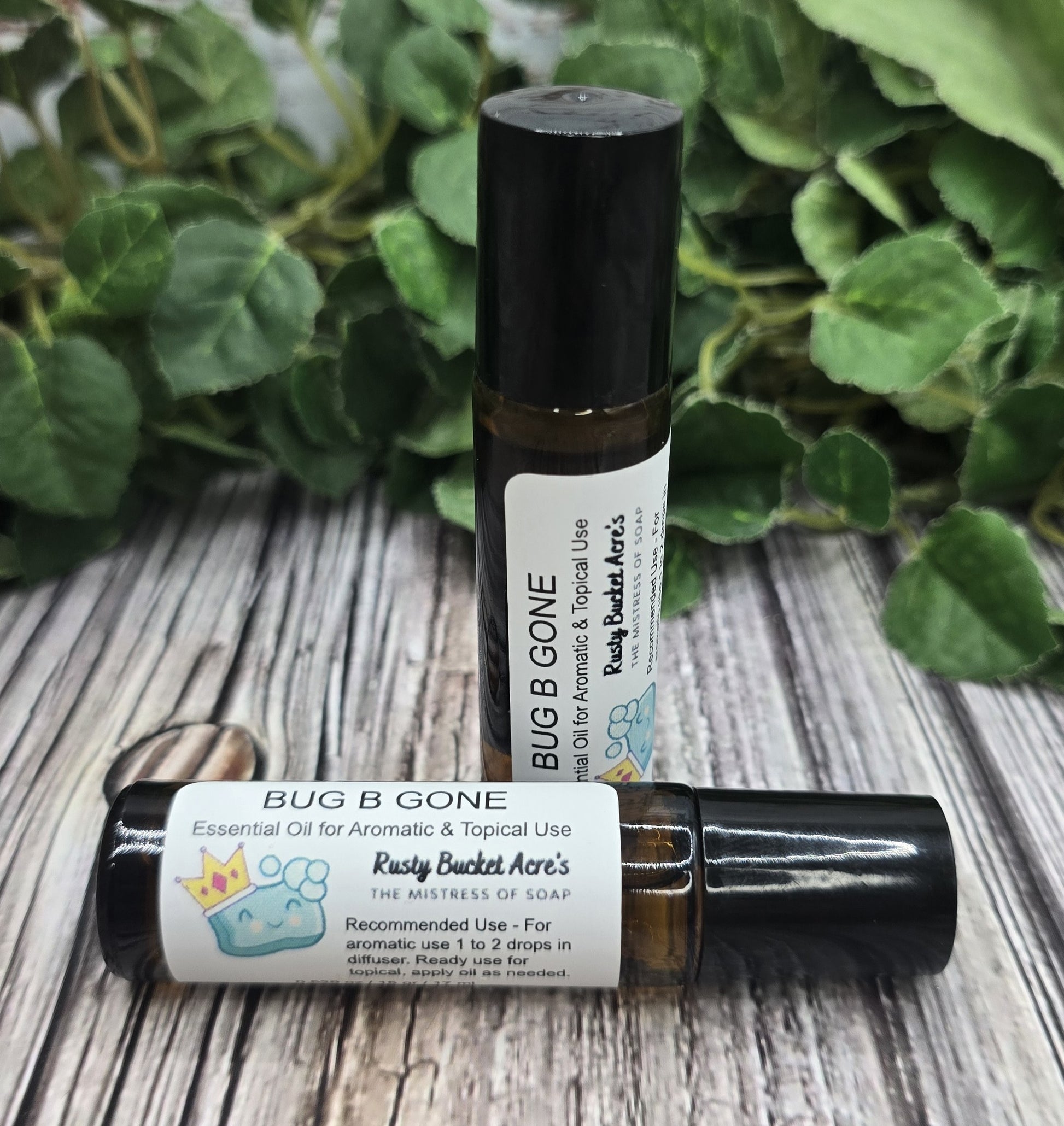 Two bottles of 'Bug B Gone' essential oil with labels on a wooden surface with green leaves in the background.