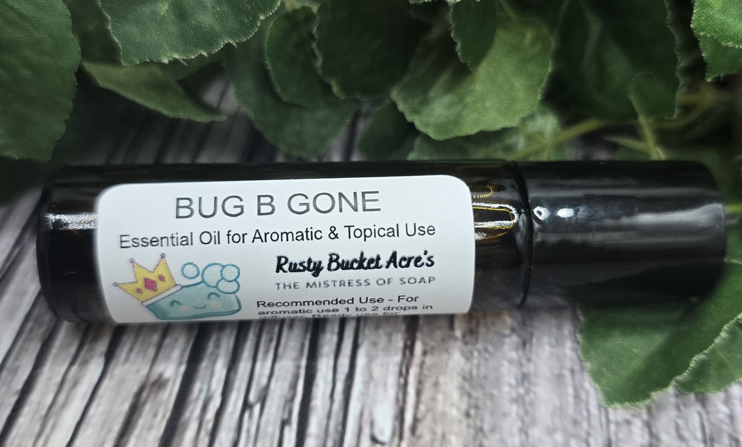 Roll-on bottle of 'Bug B Gone' essential oil with a label on a wooden surface with green leaves in the background.
