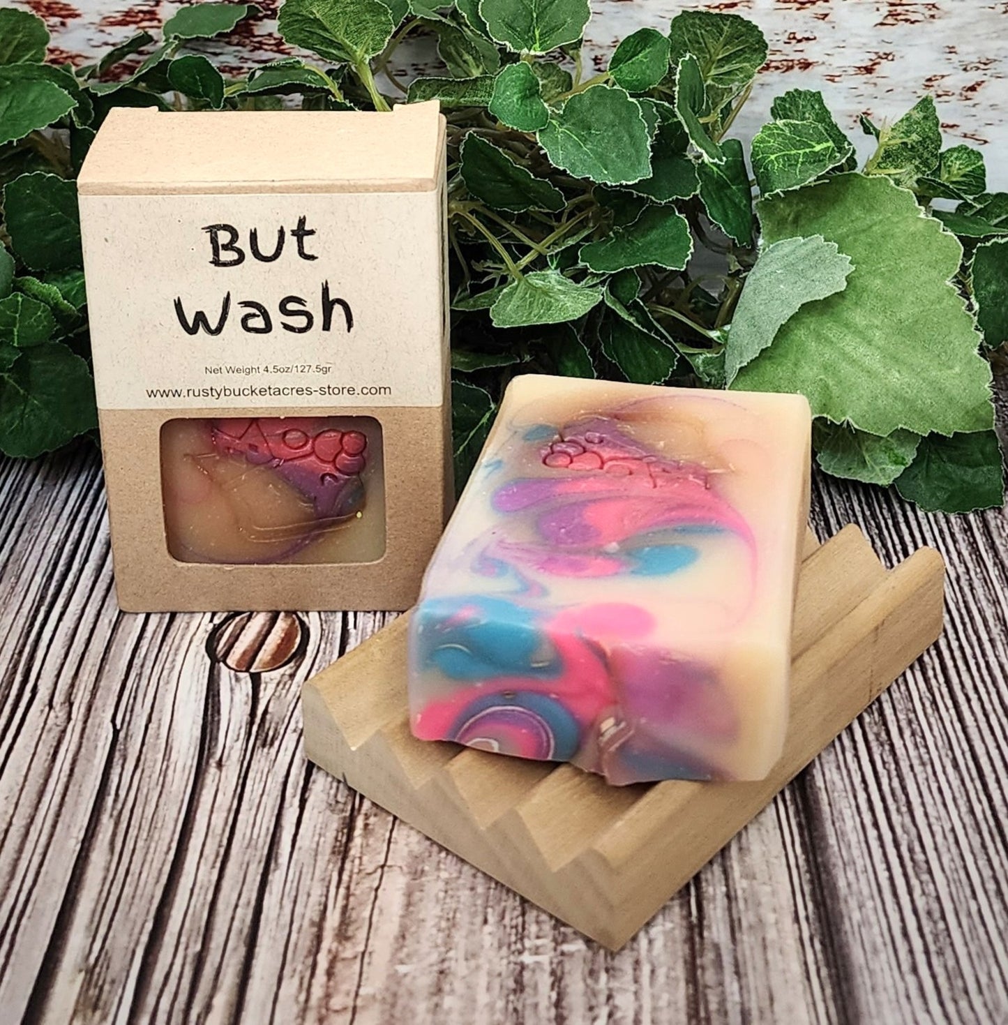 Colorful soap bar on a wooden stand with a 'But Wash' packaging in the background.