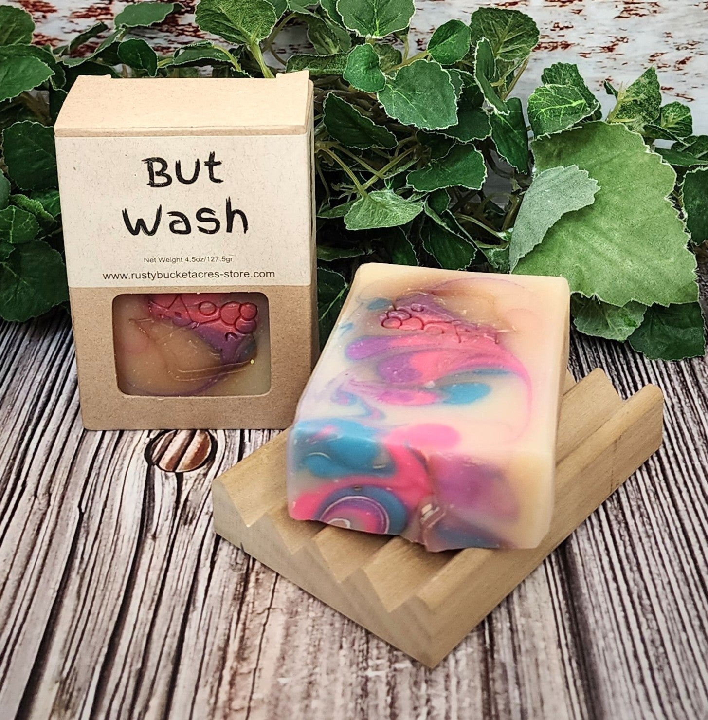 Colorful soap bar on a wooden stand with a 'But Wash' packaging in the background.