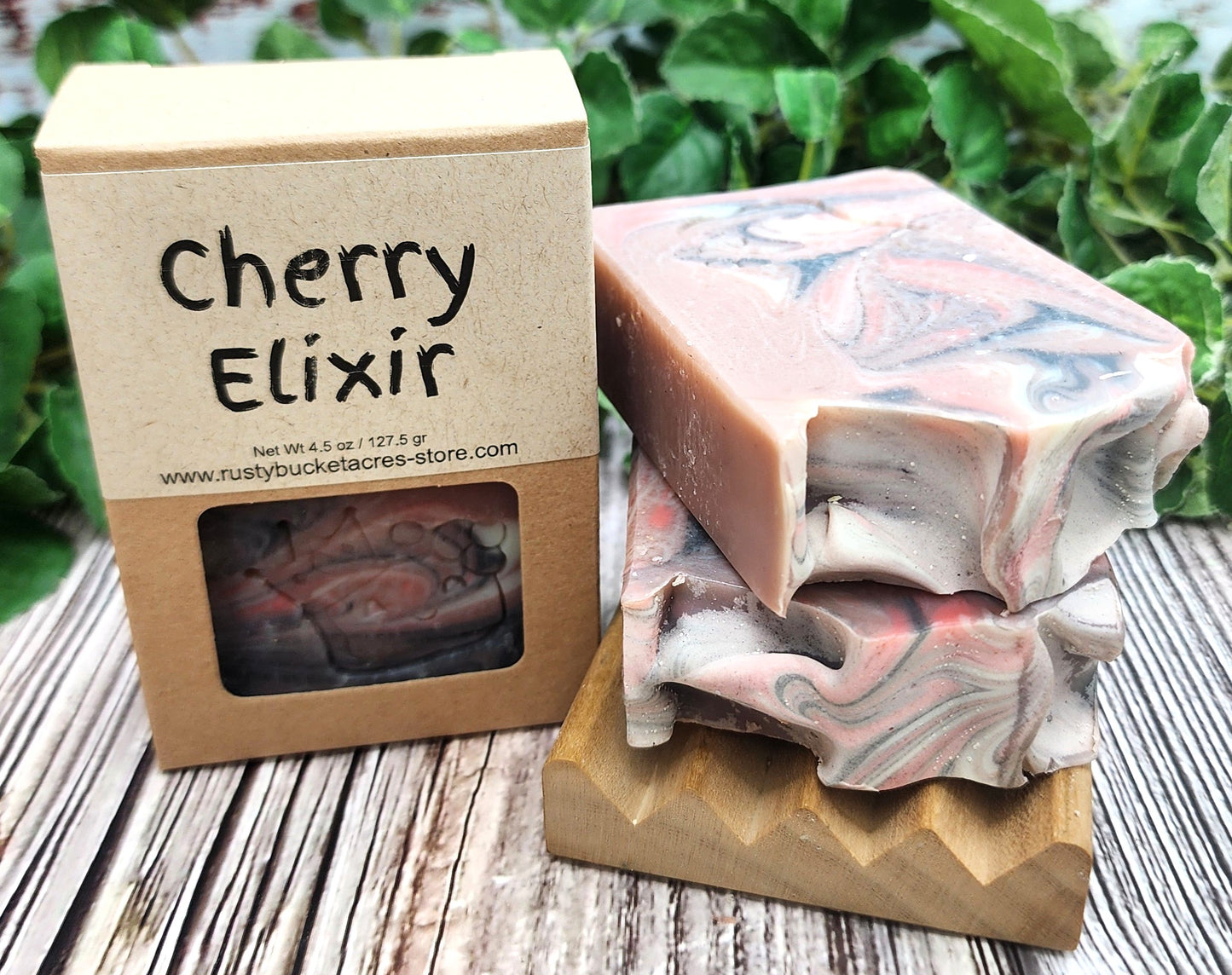 Marbled soap bars on a wooden block with a 'Cherry Elixir' soap packaging in the background.