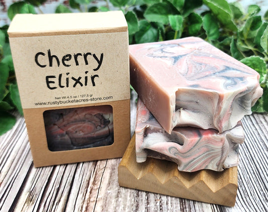 Marbled soap bars on a wooden block with a 'Cherry Elixir' soap packaging in the background.