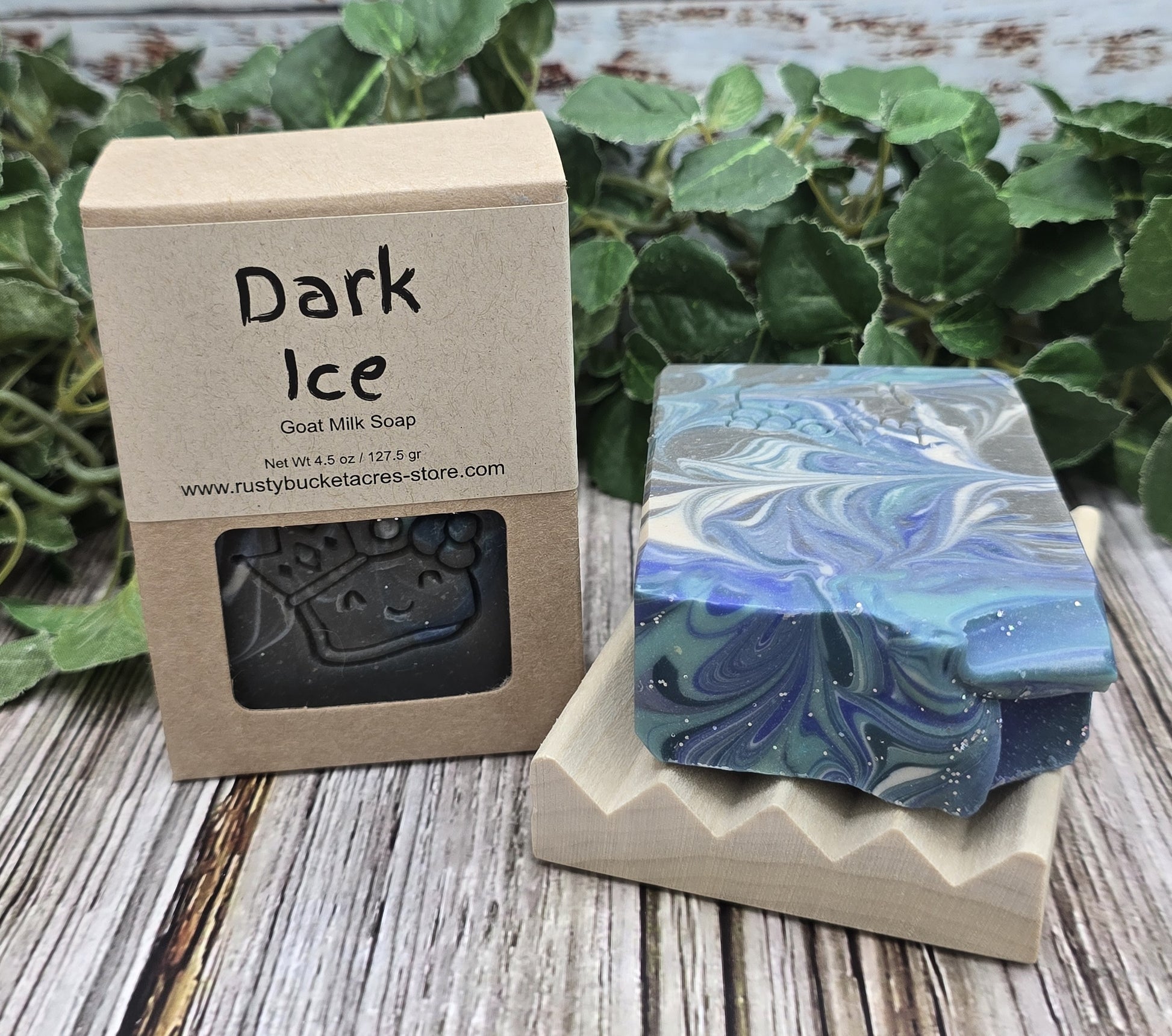 Two soap bars, one black and one with a blue and green marbled pattern, on a wooden surface with a cardboard box labeled 'Dark Ice' in the background.
