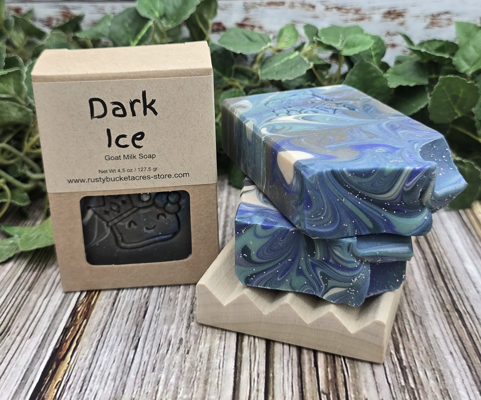 Dark Ice goat milk soap with packaging on a wooden surface with greenery in the background