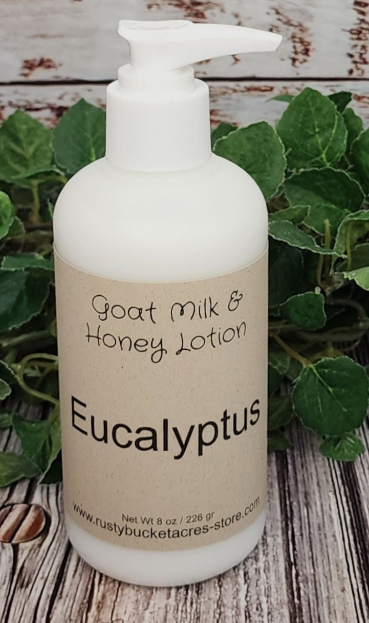 Bottle of goat milk and honey lotion labeled 'Eucalyptus' on a wooden surface with green leaves.