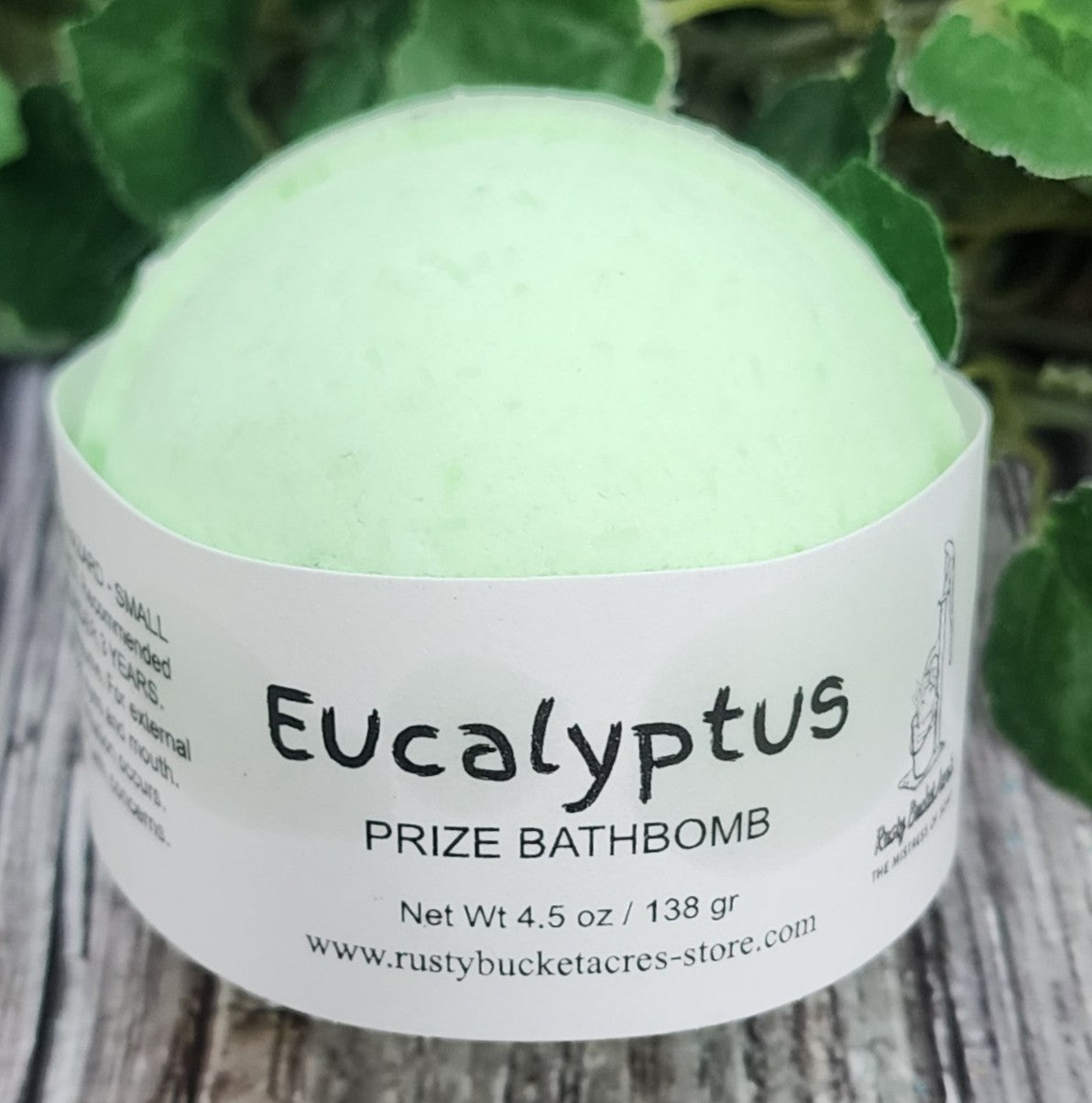 Green bath bomb with a label on a wooden surface with greenery in the background