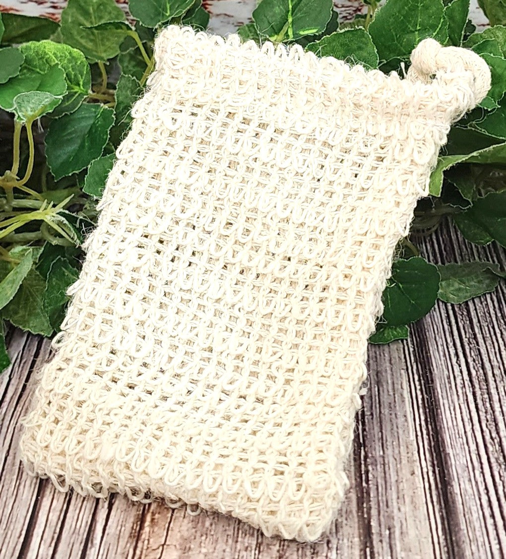 Beige woven soap bag on a wooden surface with green leaves in the background