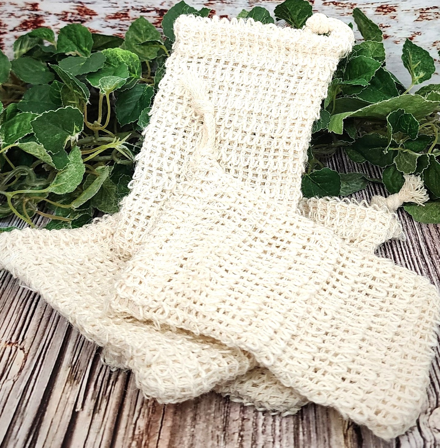 beige exfoliating bags on a wooden surface with green leaves in the background