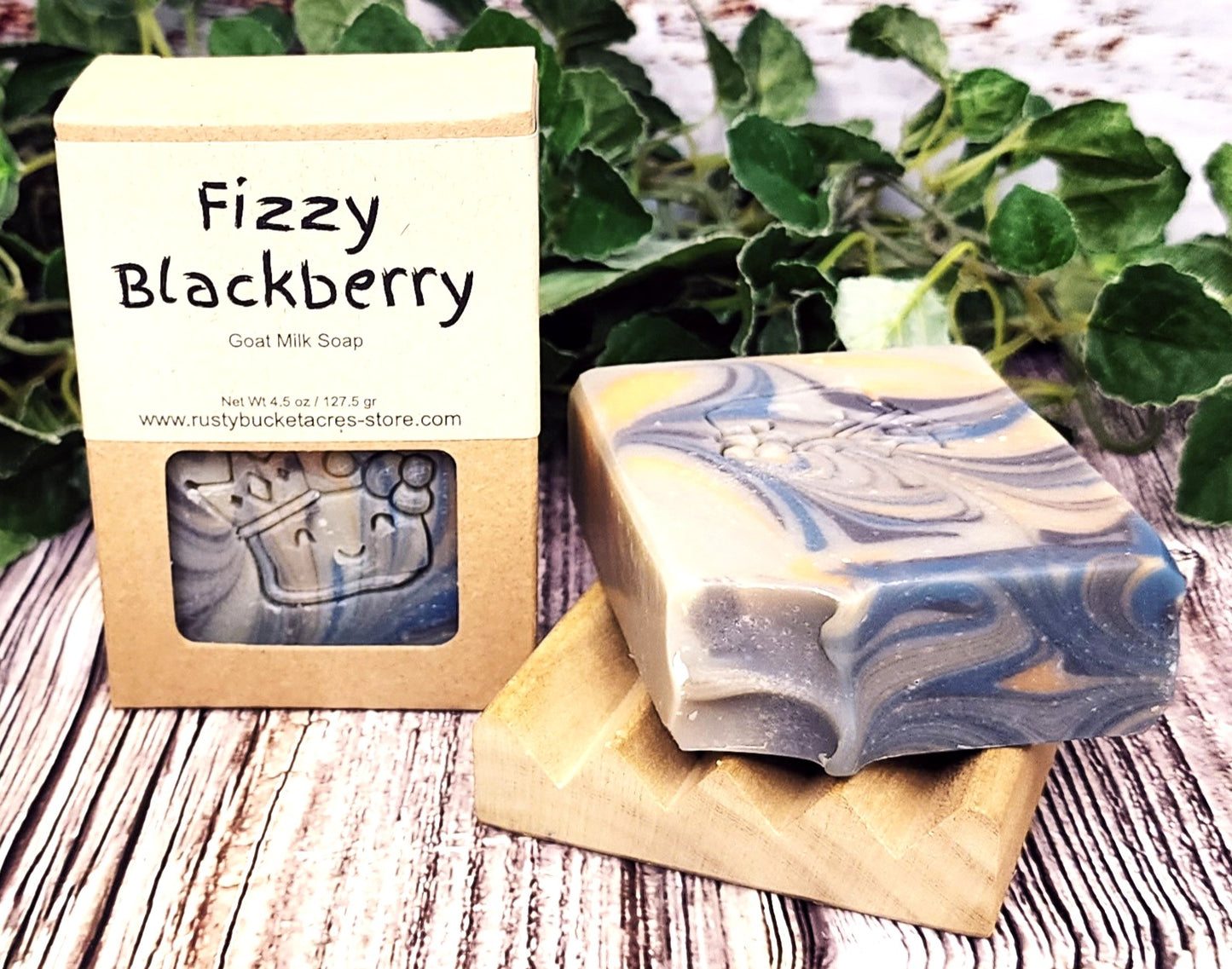 Fizzy Blackberry soap bar with packaging on a wooden surface with green leaves in the background