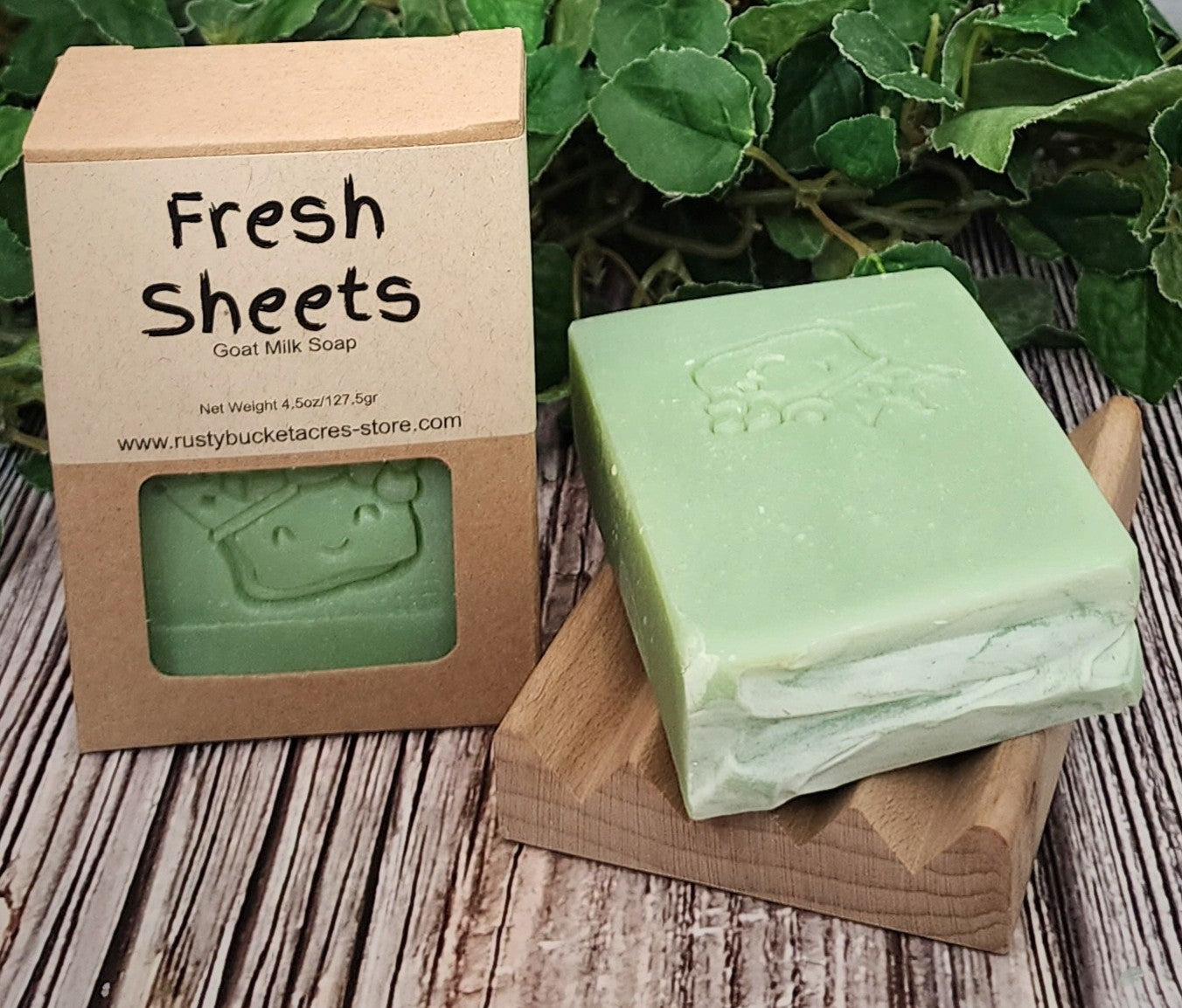 Green bar of soap on a wooden block with a 'Fresh Sheets' soap packaging in the background.