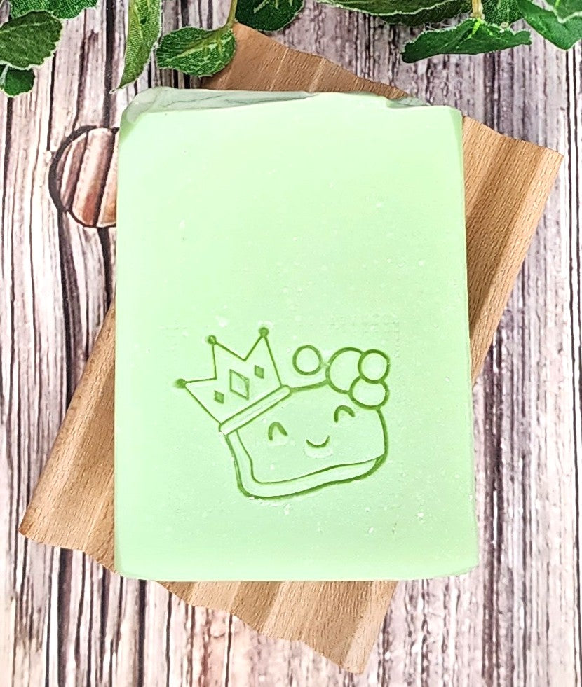 Green soap bar with a crown design on a wooden soap dish against a wooden background.